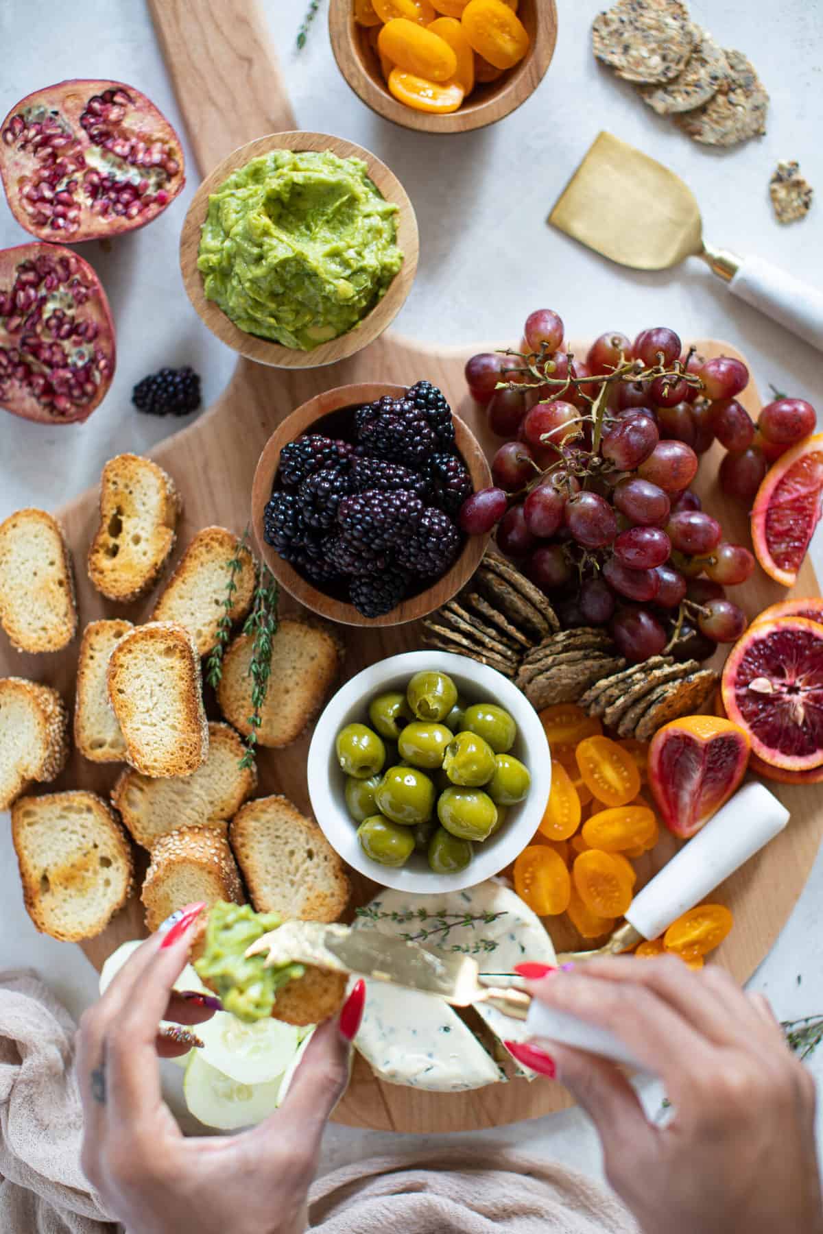 Woman spreading guacamole on a cracker over a charcuterie board.