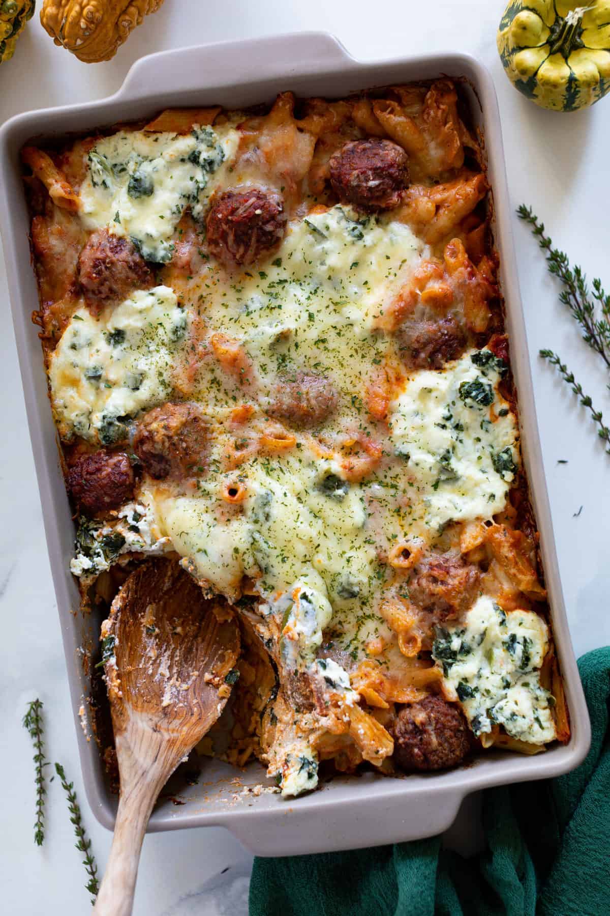 Wooden spoon in a baking dish of gluten-free Baked Meatball Penne Pasta Casserole.