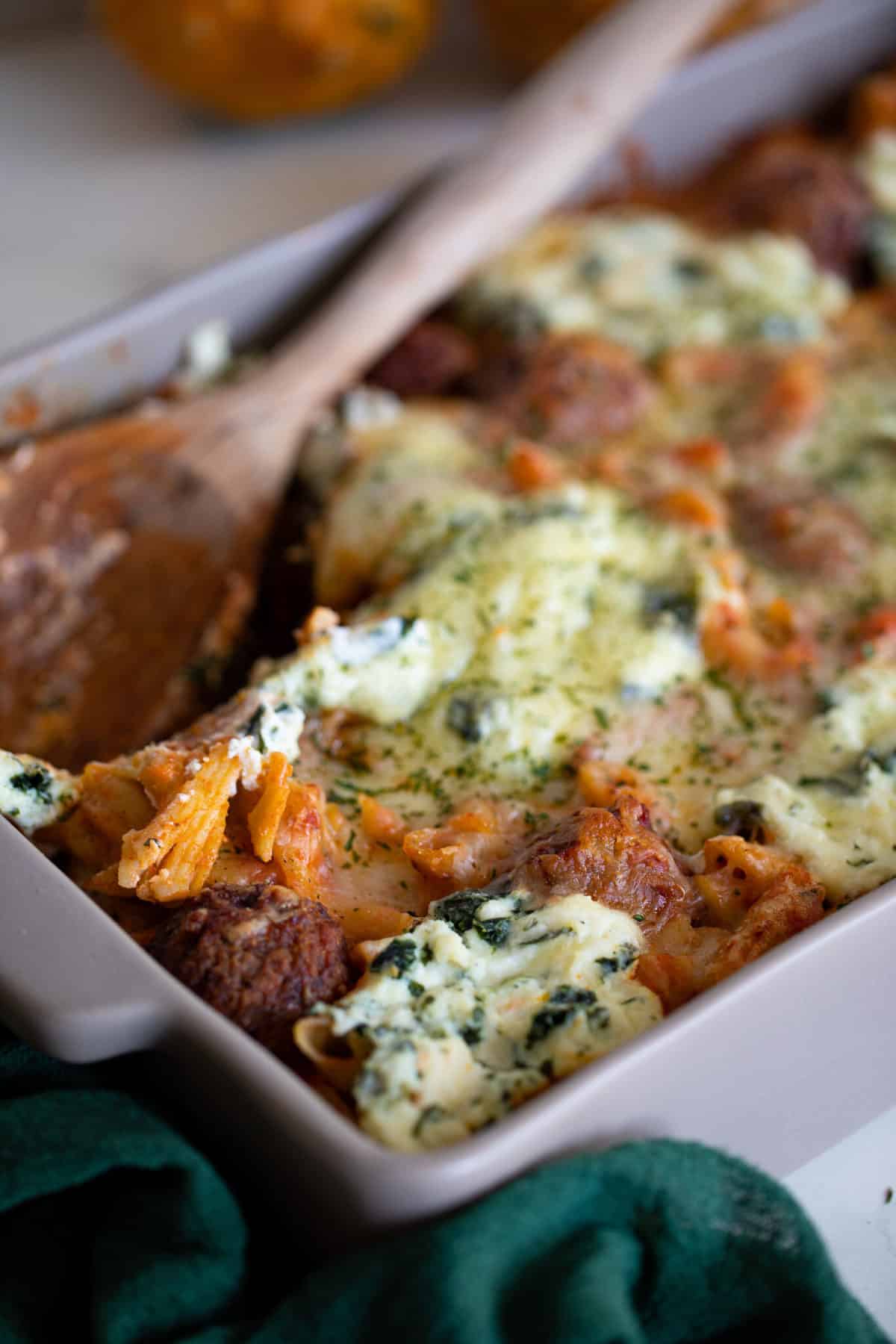 Wooden spoon in a baking dish of gluten-free Baked Meatball Penne Pasta Casserole.