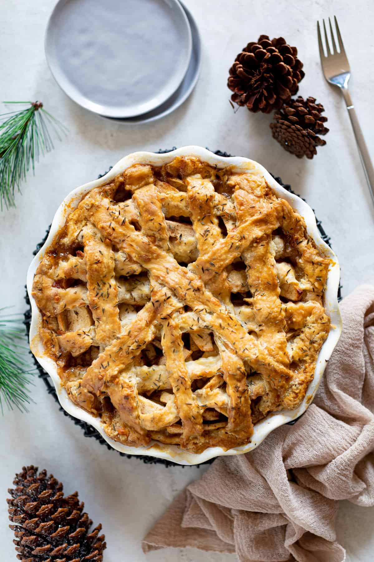 Apple Cheddar Thyme Pie on a table with pinecones and evergreen branches.