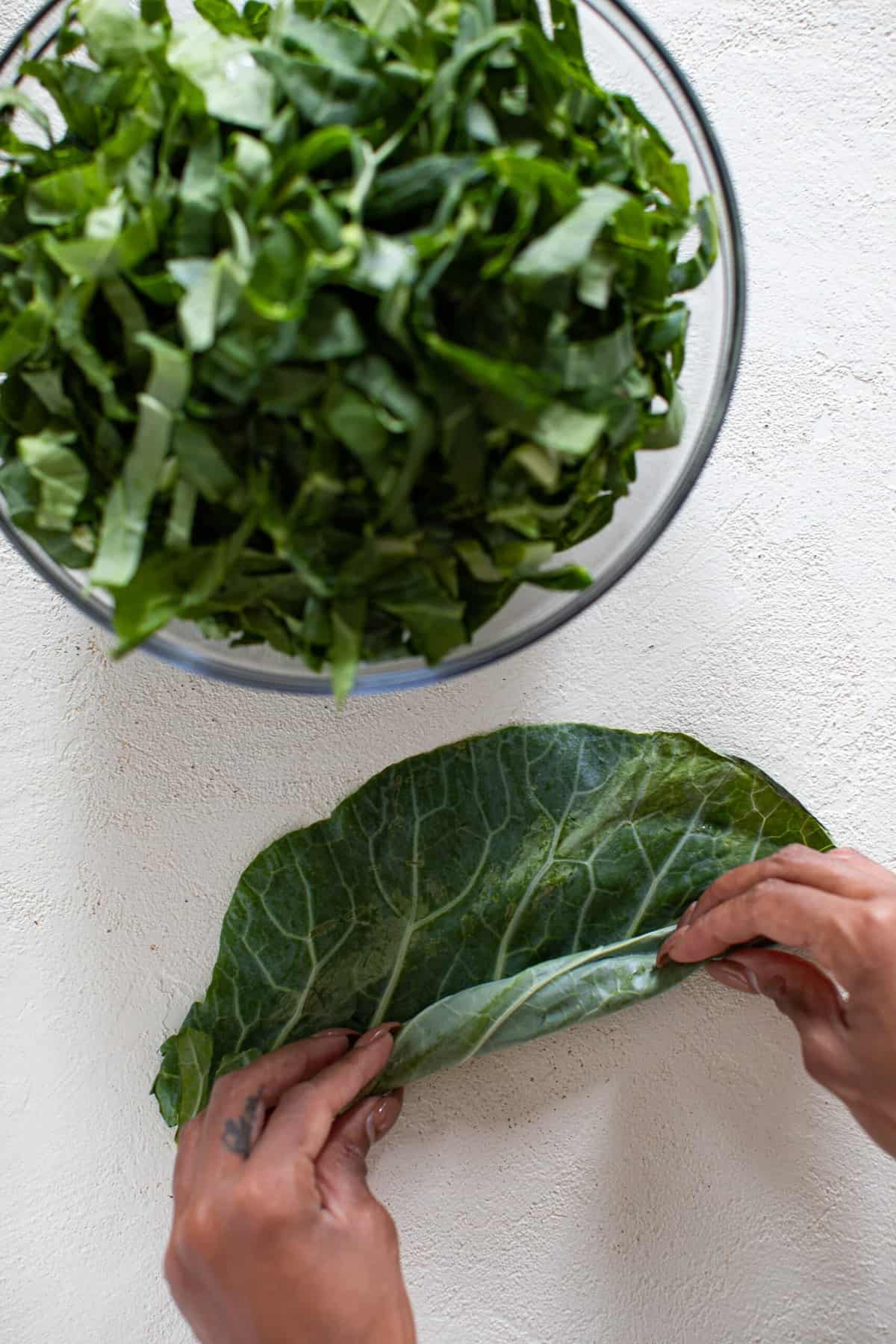 Hands rolling collard greens next to a bowl of chopped collard greens