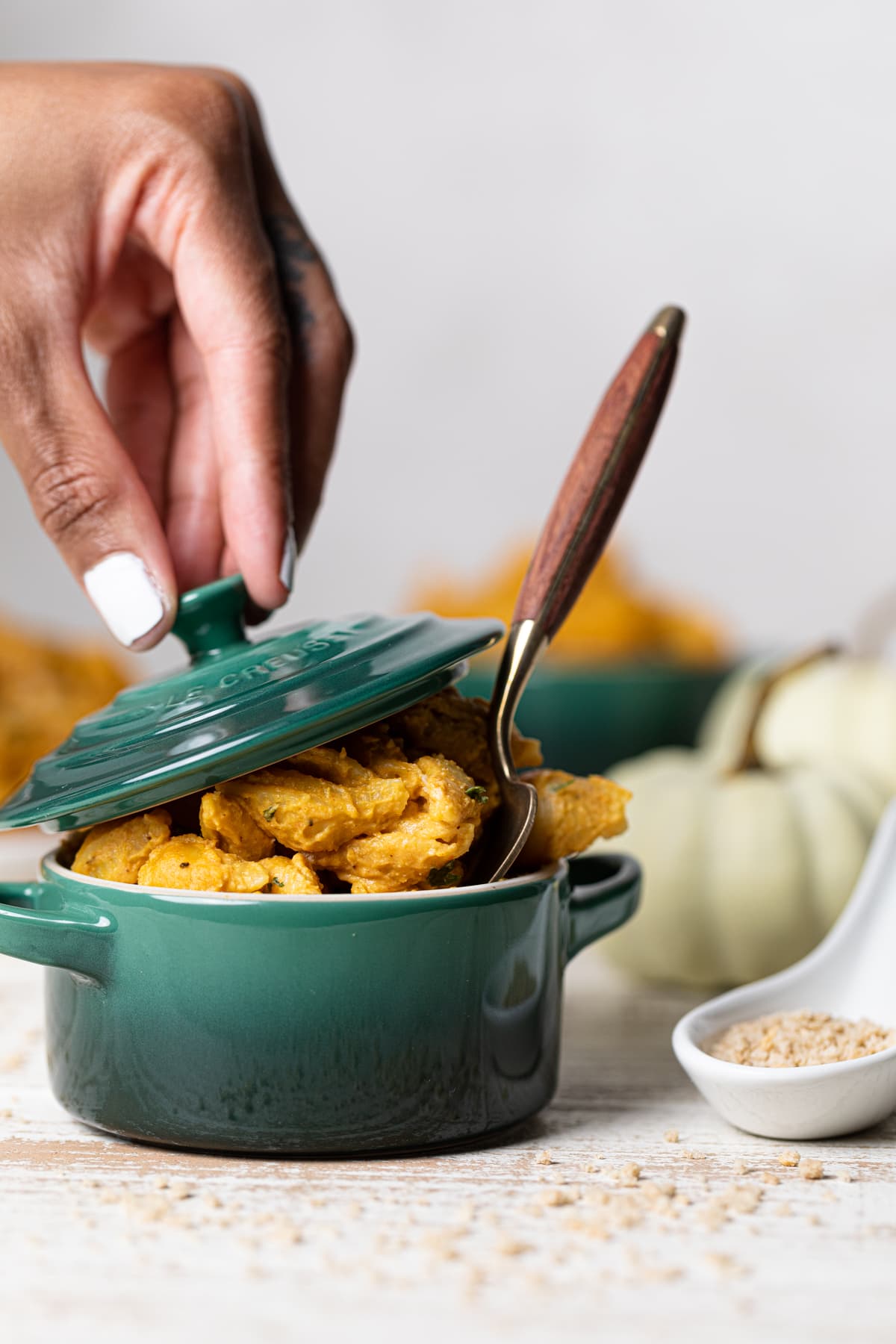 Hand holding the lid over a mini cocotte of Vegan Pumpkin Mac and Cheese