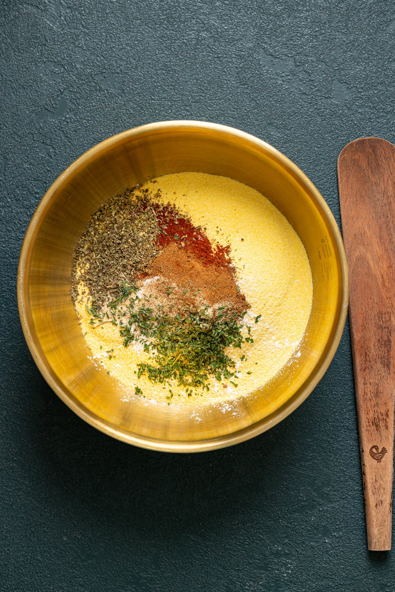 Ingredients in a gold bowl with a wooden spatula.