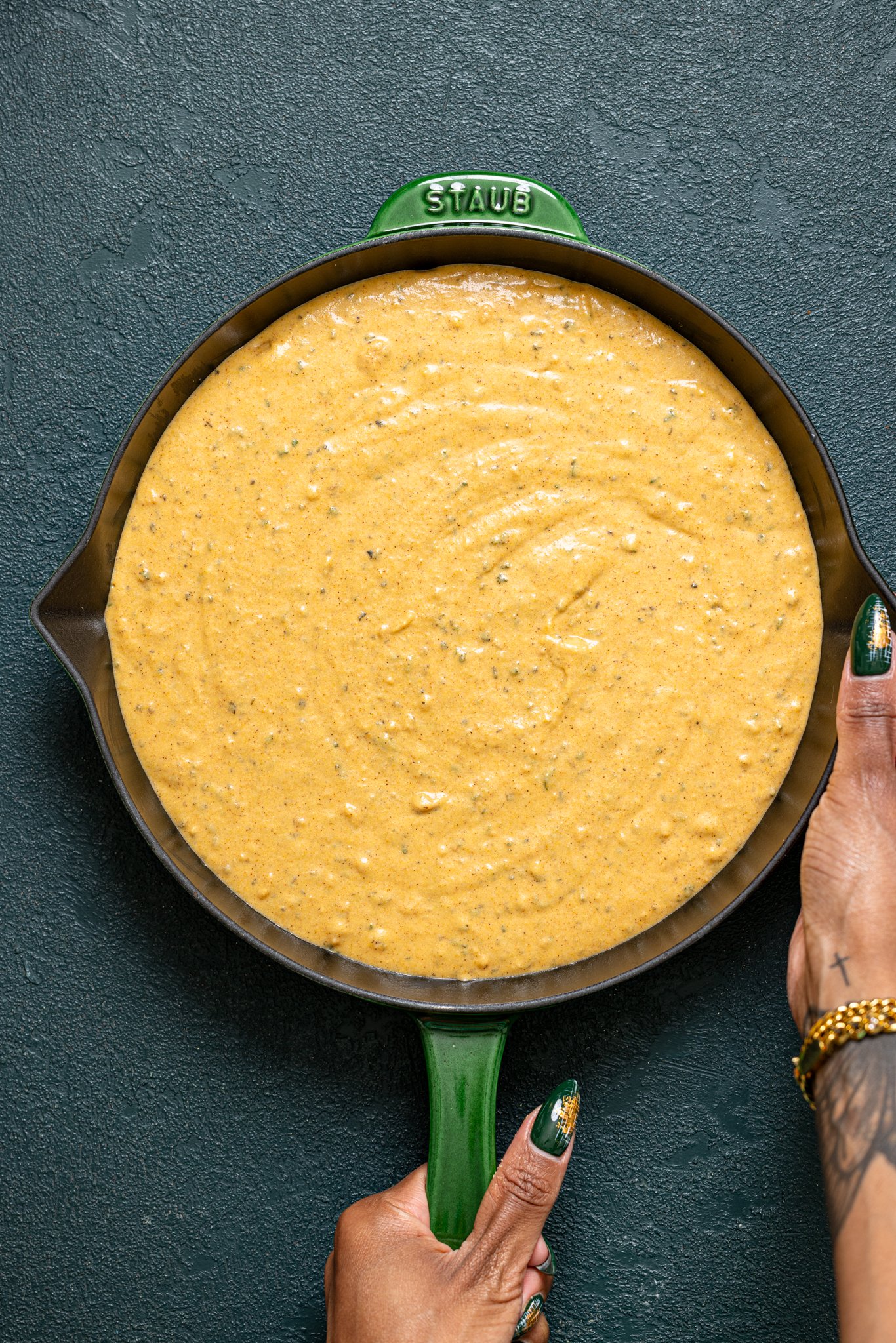 Batter in a skillet being held by woman hands.