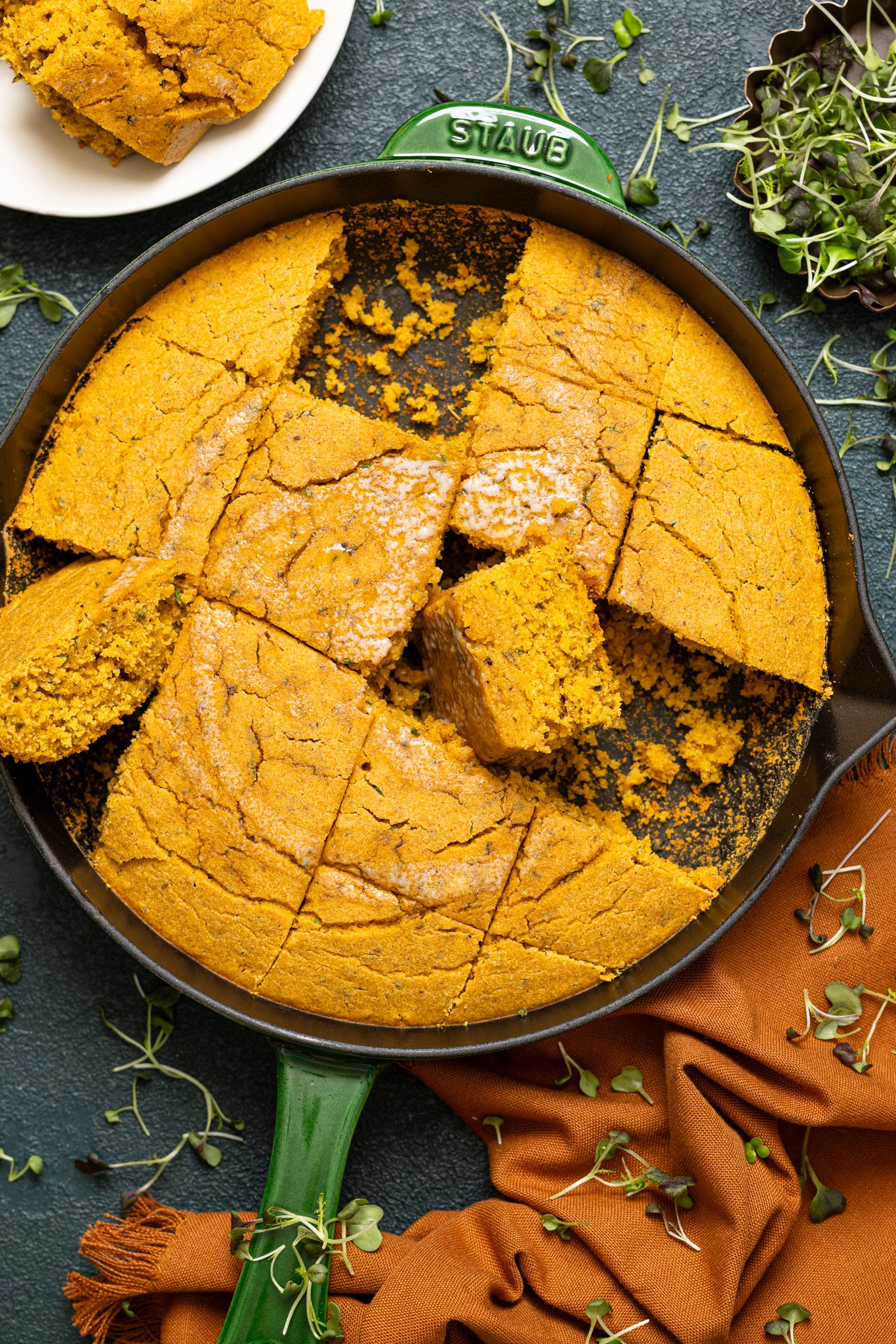Vegan Sweet Potato Maple Herb Cornbread in a skillet on a hunter green table.