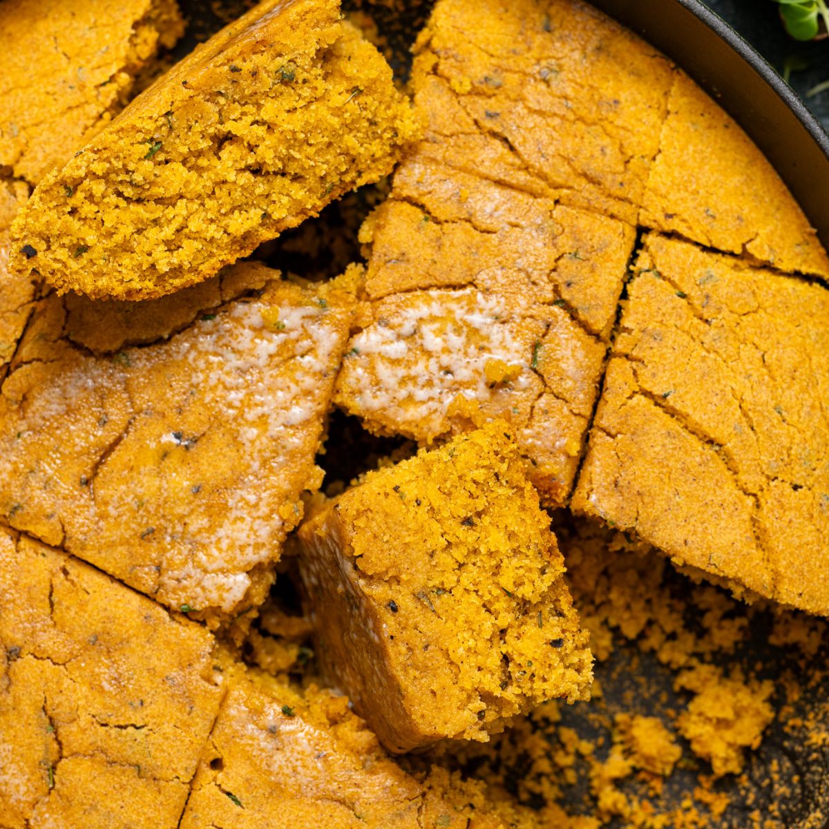 Up close shot of Vegan Sweet Potato Maple Herb Cornbread sliced in a skillet.