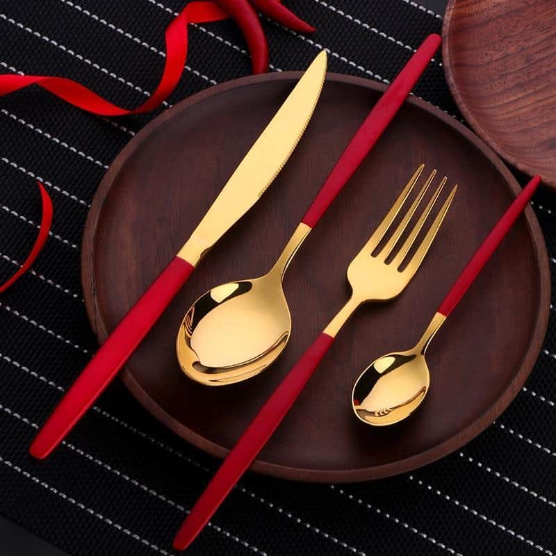 Golden and red silverware on a wooden plate.