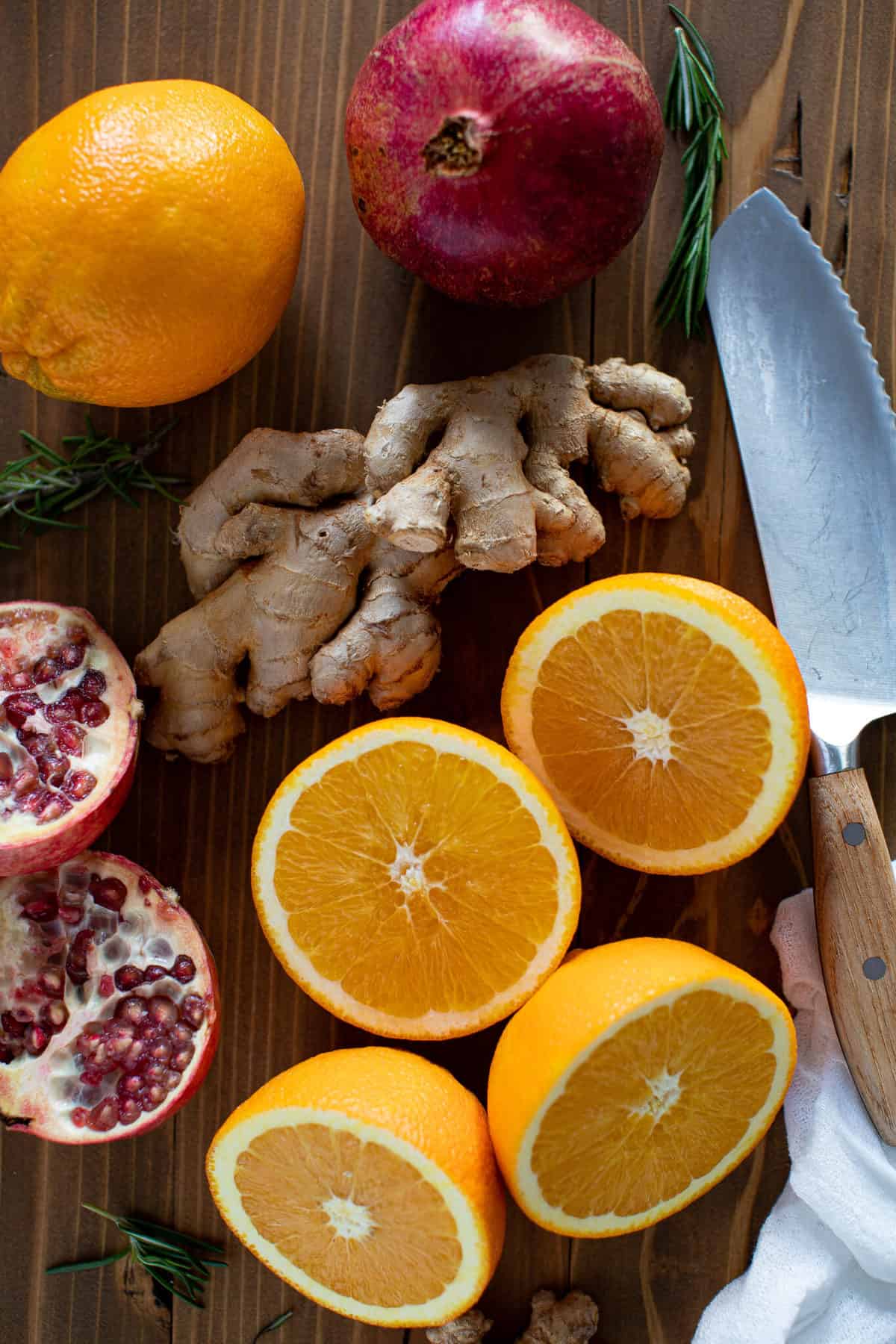 Ginger, orange, and pomegranate halves on a wooden board with a knife.