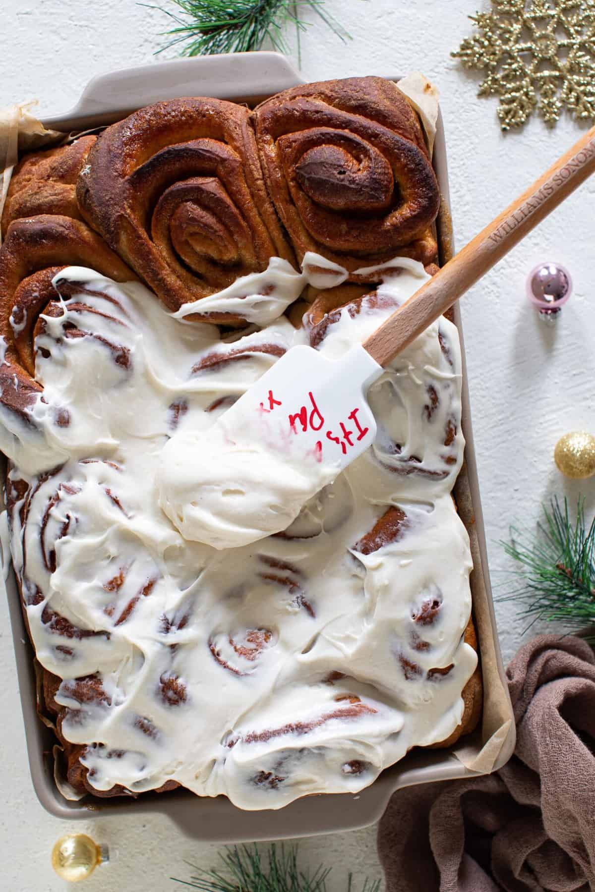 Spatula spreading icing onto Apple Butter Eggnog Cinnamon Rolls.