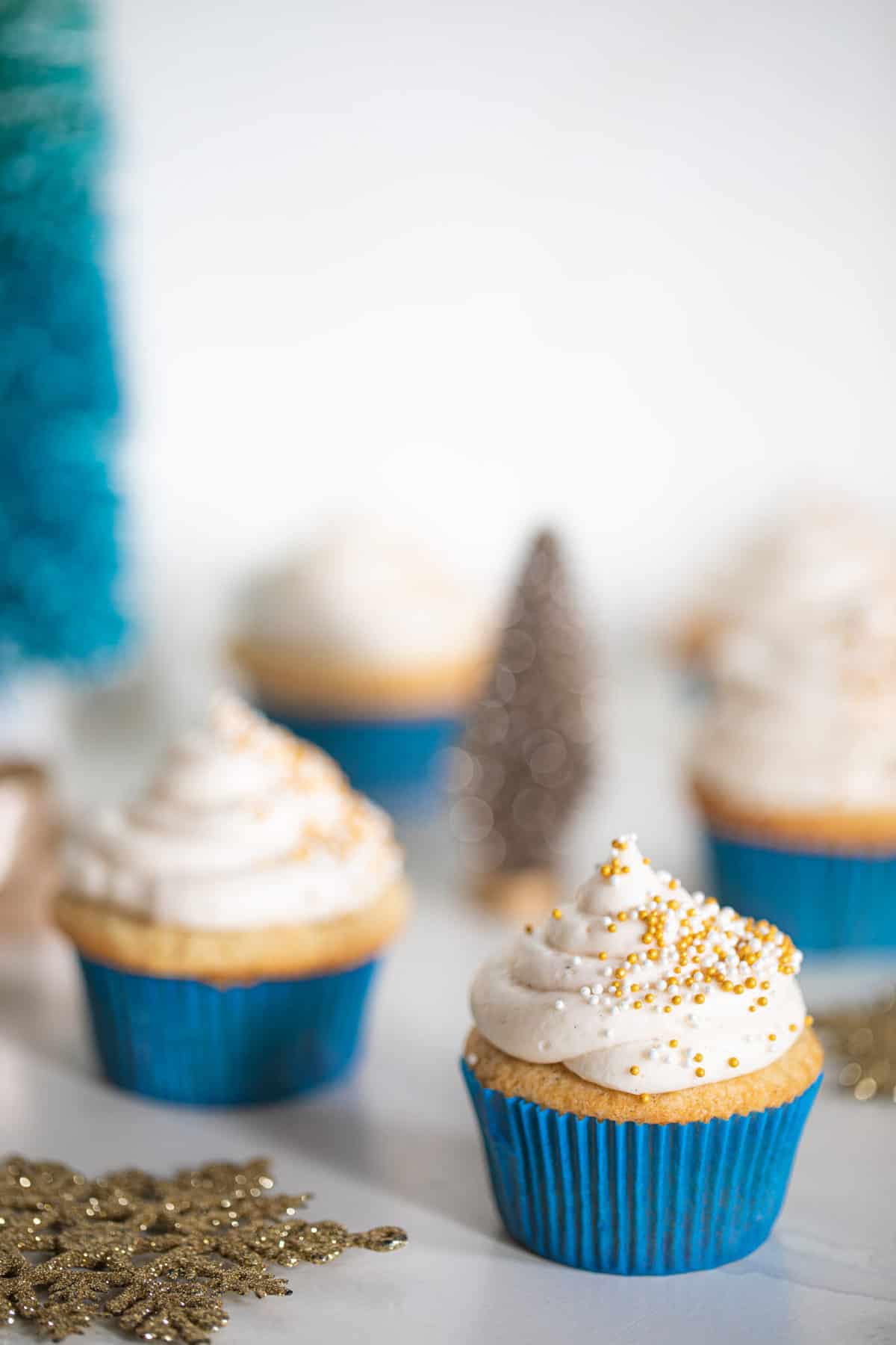 Eggnog Cupcakes with Cream Cheese Frosting around a small, decorative Christmas tree.