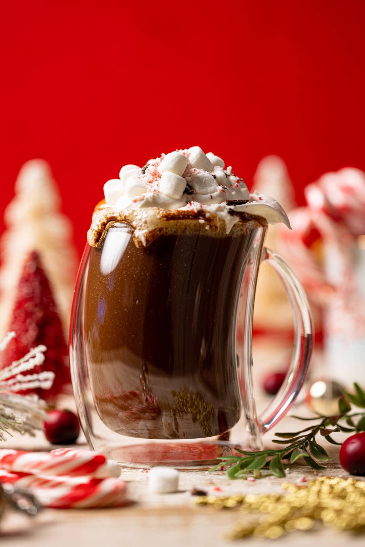 Homemade Peppermint Mocha Latte in a lopsided glass topped with whipped cream and marshmallows near a pile of candy canes