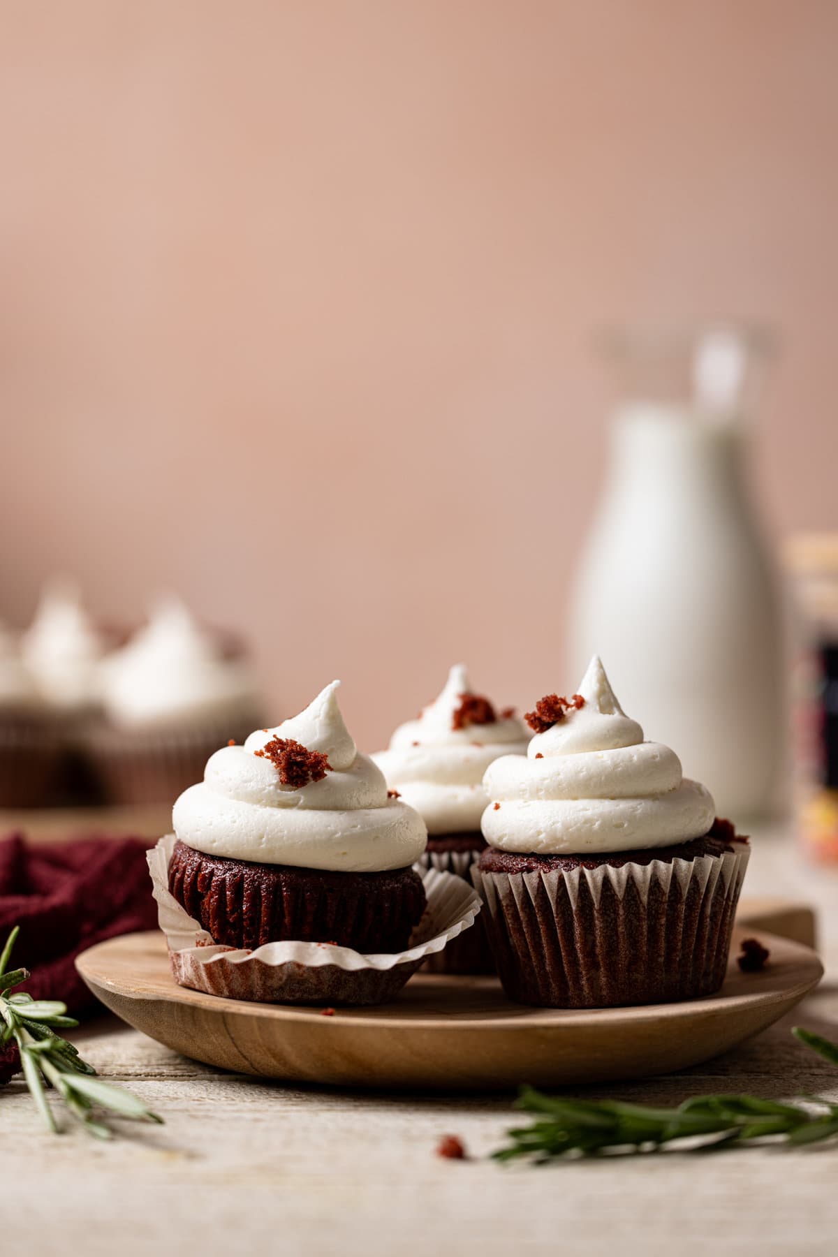 Three Vegan Red Velvet Cupcakes with Bourbon Vanilla Buttercream on a small, wooden plate.