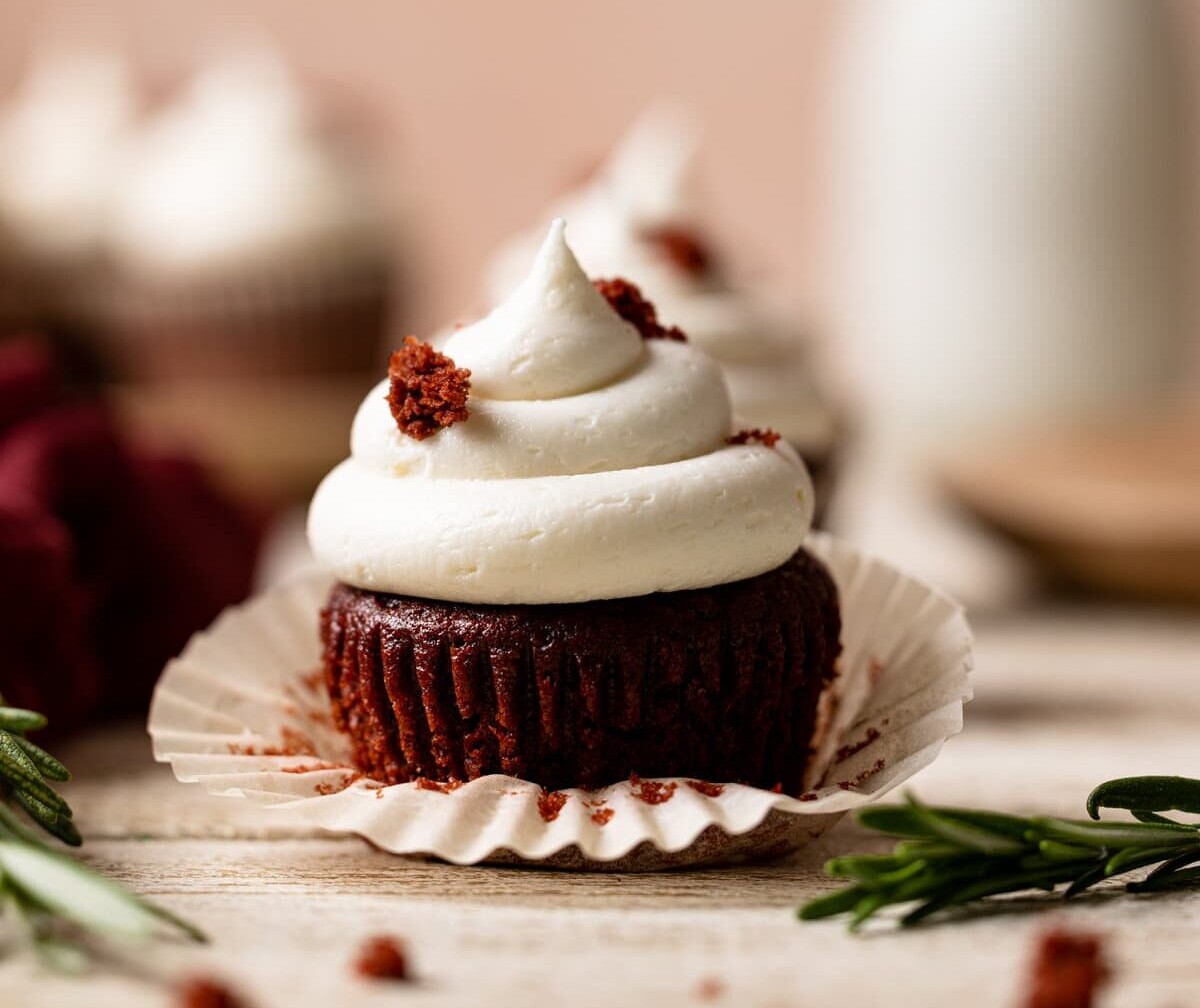 Muffin liner being removed from a Vegan Red Velvet Cupcake with Bourbon Vanilla Buttercream.