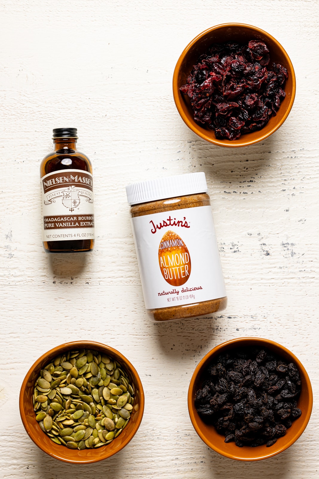 Ingredients on a white table including almond butter, vanilla, pumpkin seeds, cranberries, etc.