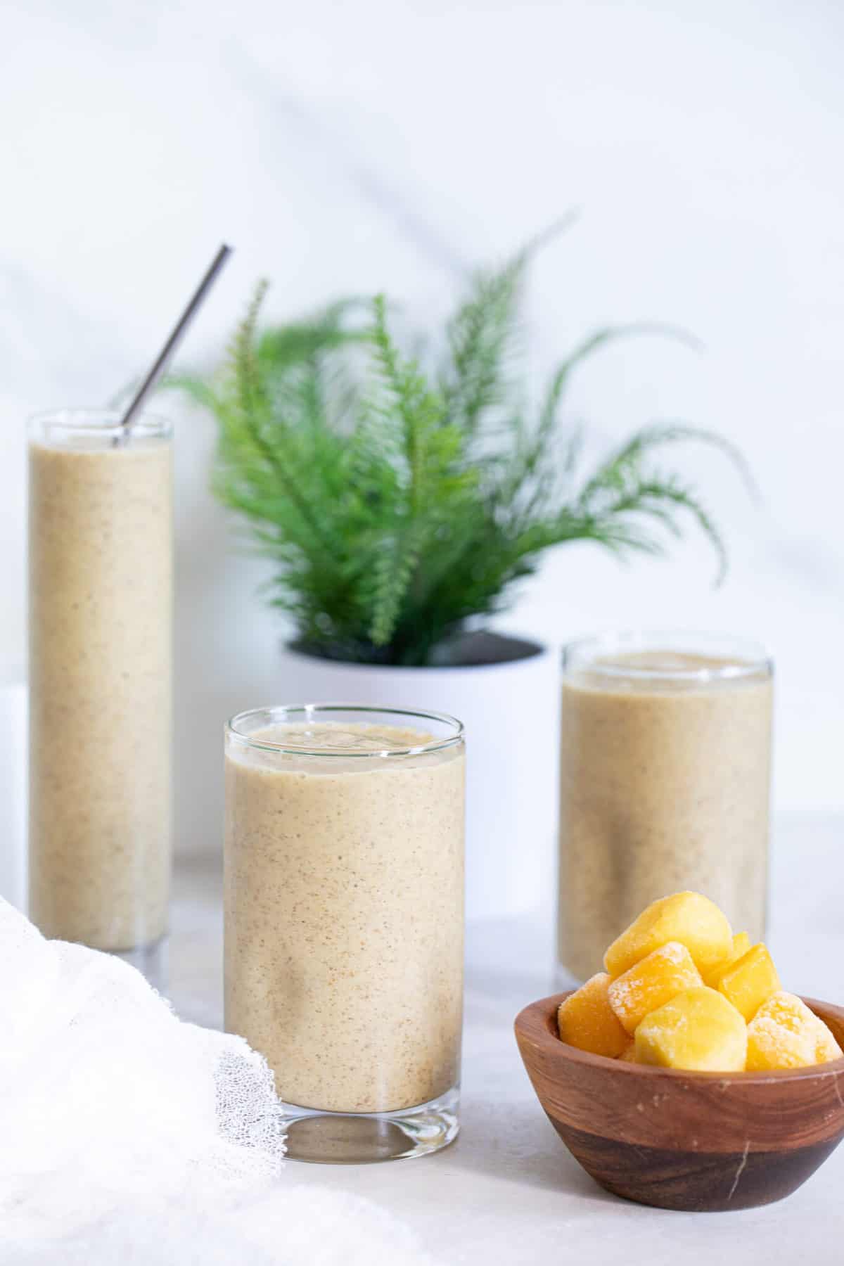 Three glasses of Mango Chia Seed Smoothie with a bowl of frozen mango.