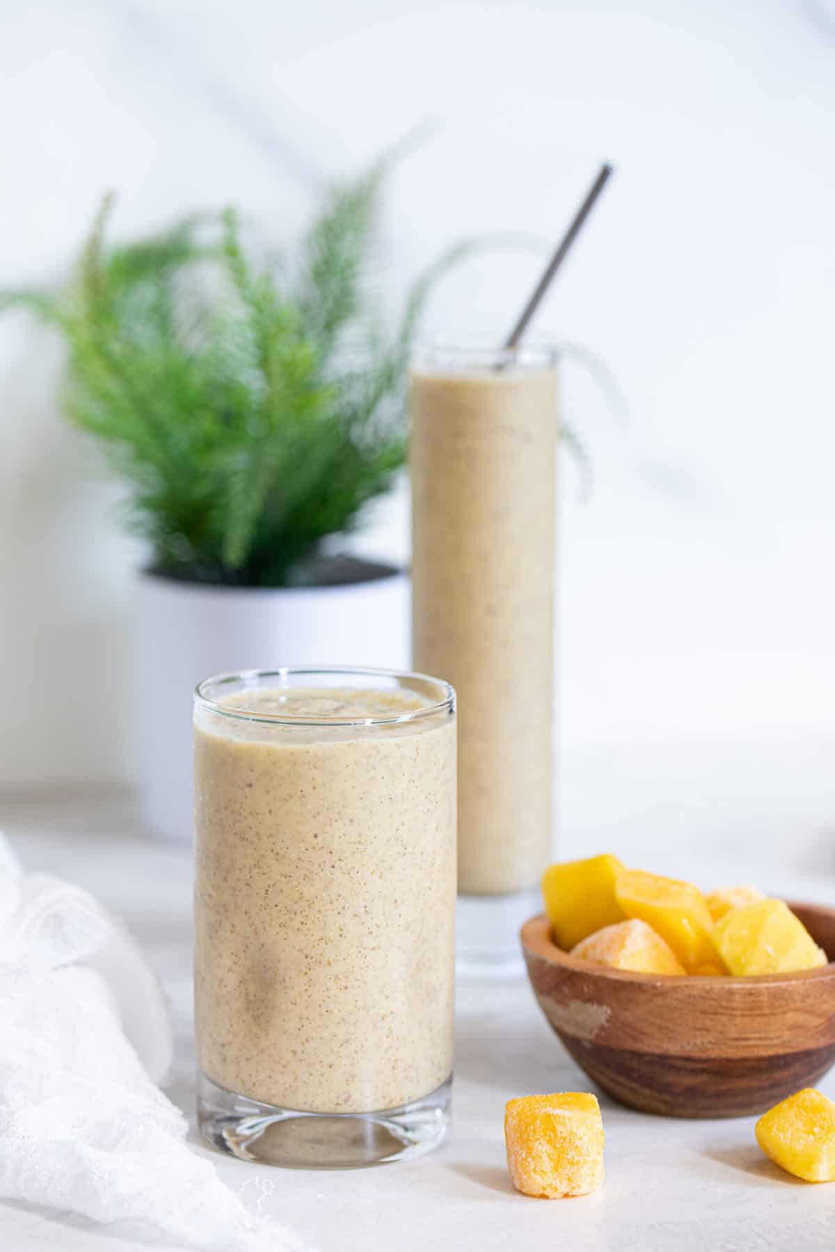 Two glasses of Mango Chia Seed Smoothie with a bowl of frozen mango.