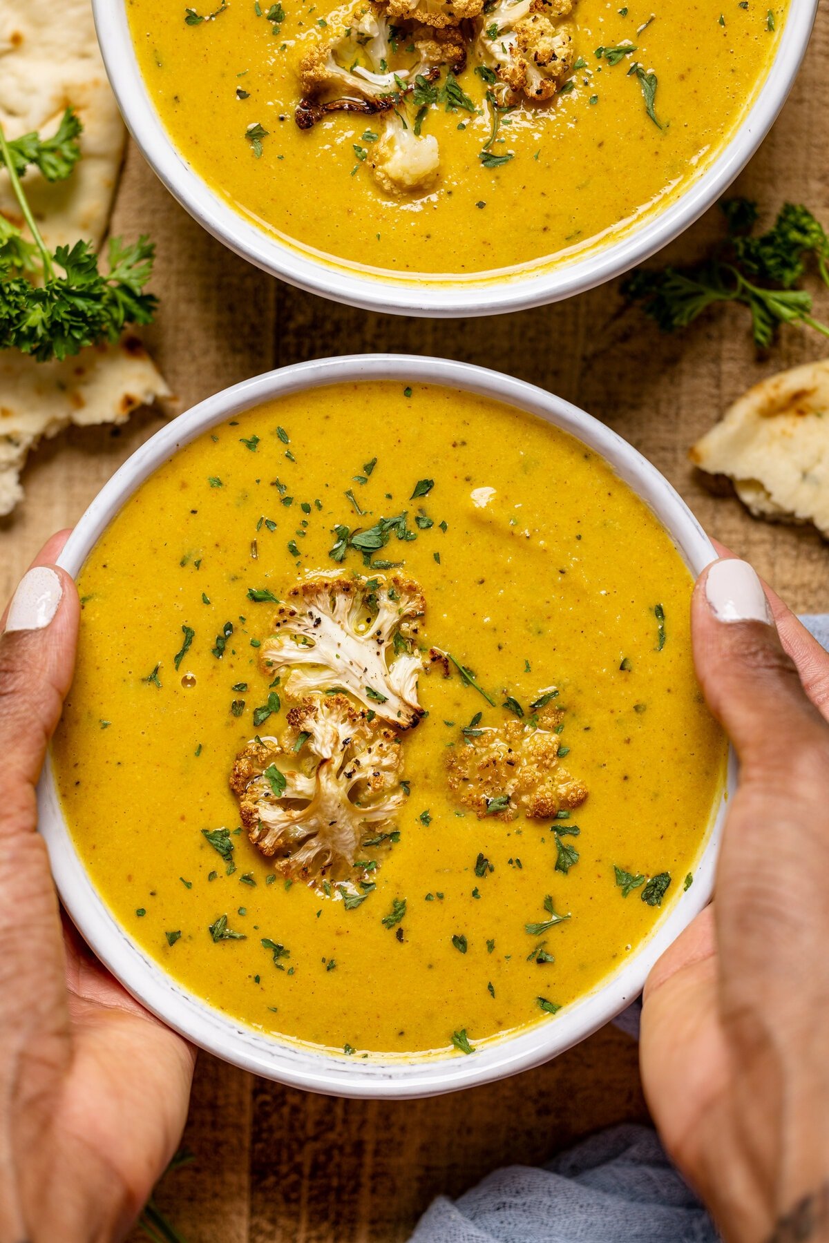 Two hands holding a bowl of Creamy Roasted Garlic Cauliflower Chickpea Soup