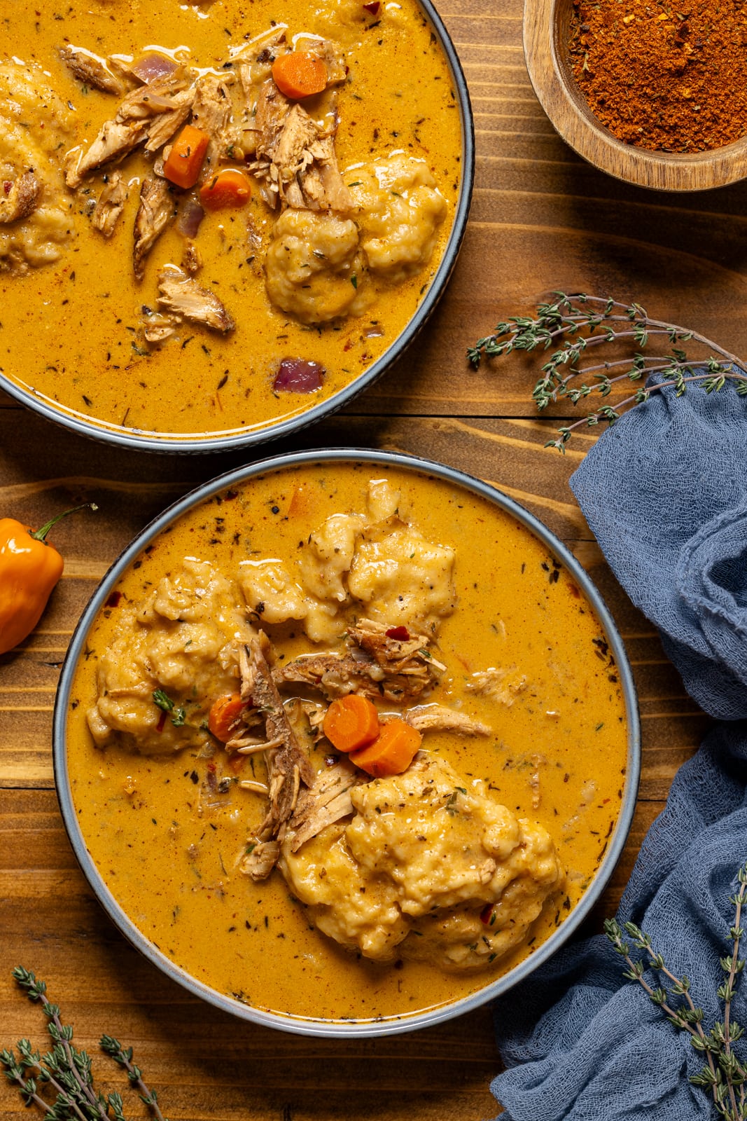 Two bowls of chicken and dumplings on a brown wood table.