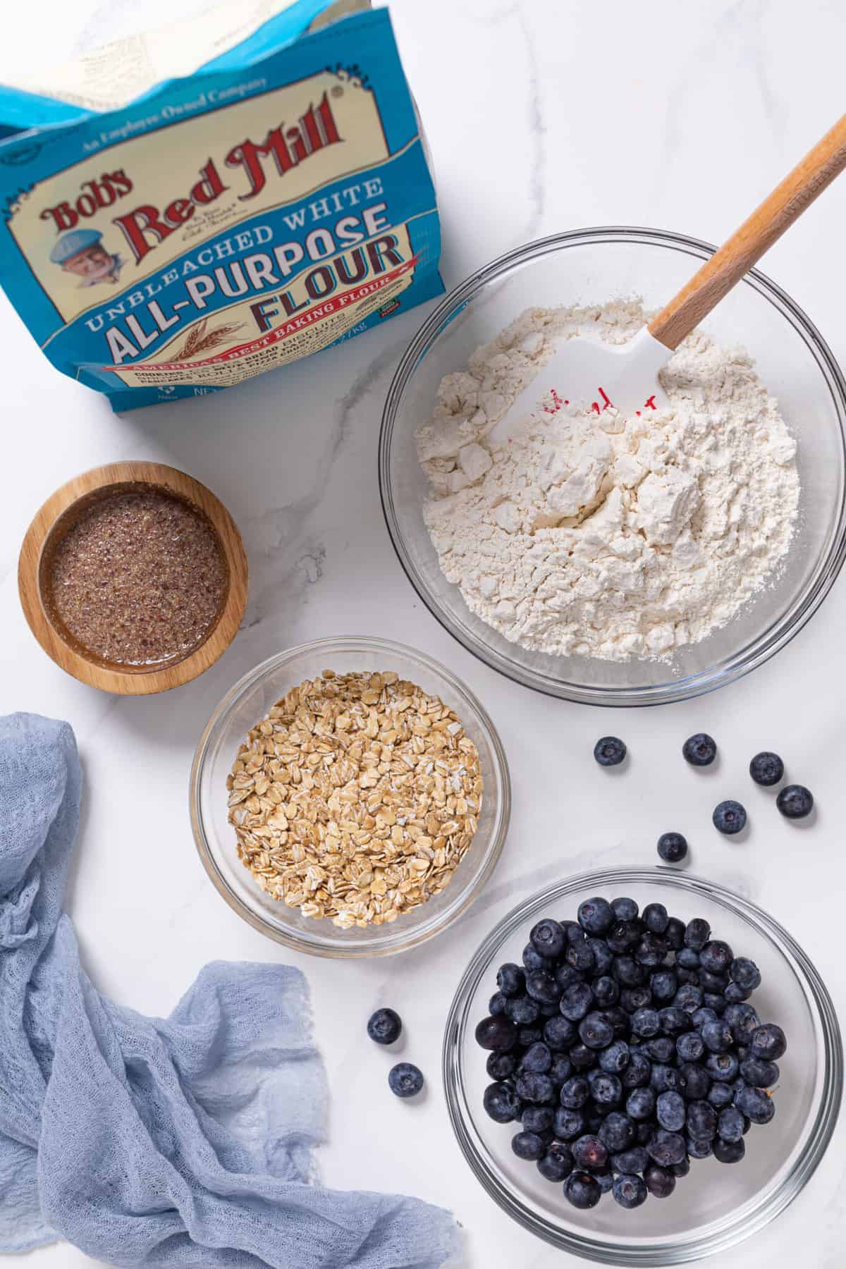 Bowls of flour, oats, blueberries, and other ingredients.