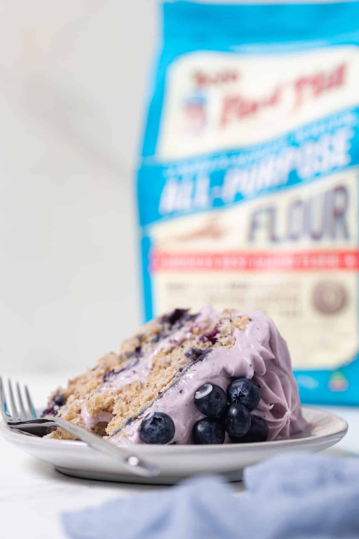 Slice of Blueberry Oatmeal Cake with Cream Cheese Frosting in front of a bag of Bob\'s Red Mill flour.