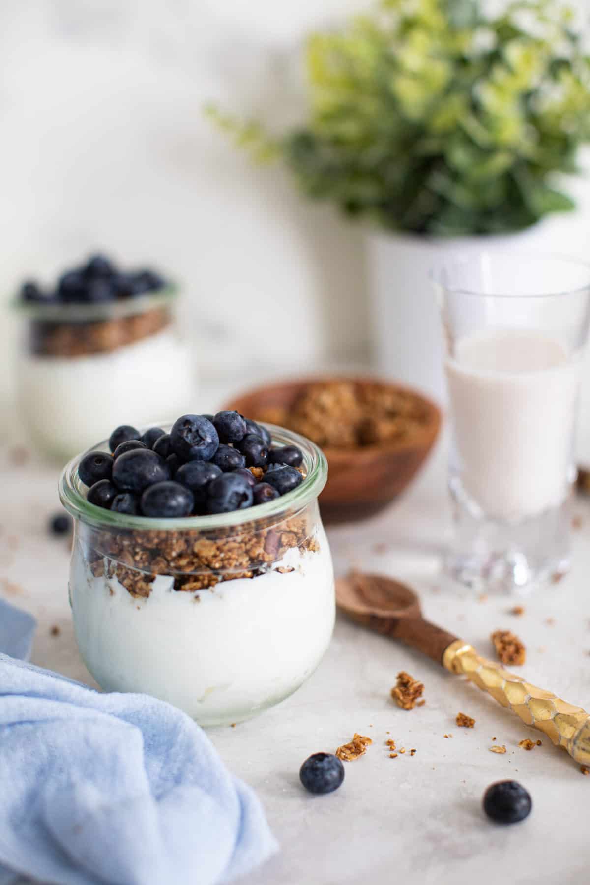 Blueberry Granola Yogurt Breakfast Parfaits on a white background with fresh berries and a blue napkin and a wooden spoon.