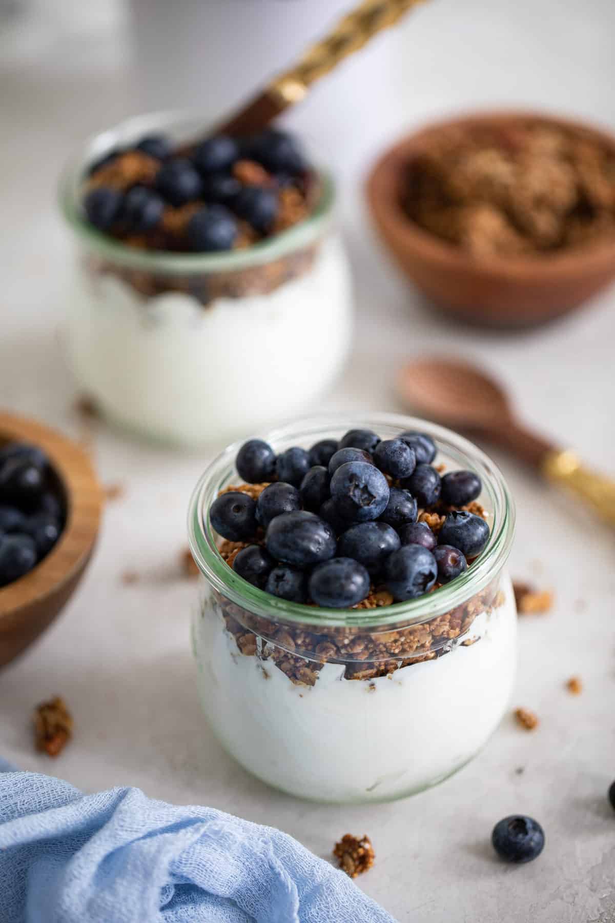 Blueberry Granola Yogurt Breakfast Parfaits on a white background with fresh berries and a blue napkin.