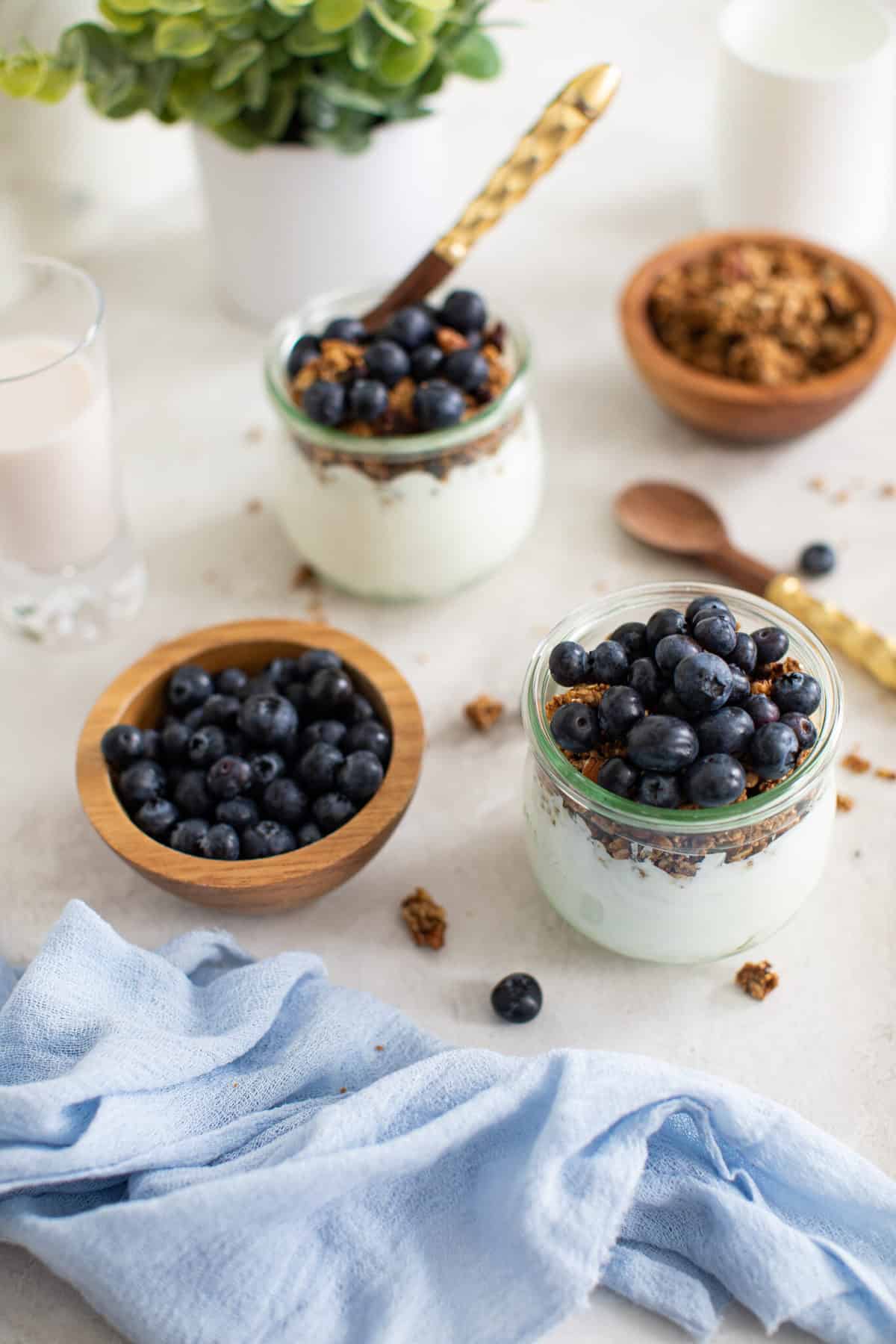 Blueberry Granola Yogurt Breakfast Parfaits on a white background with fresh berries and a blue napkin.