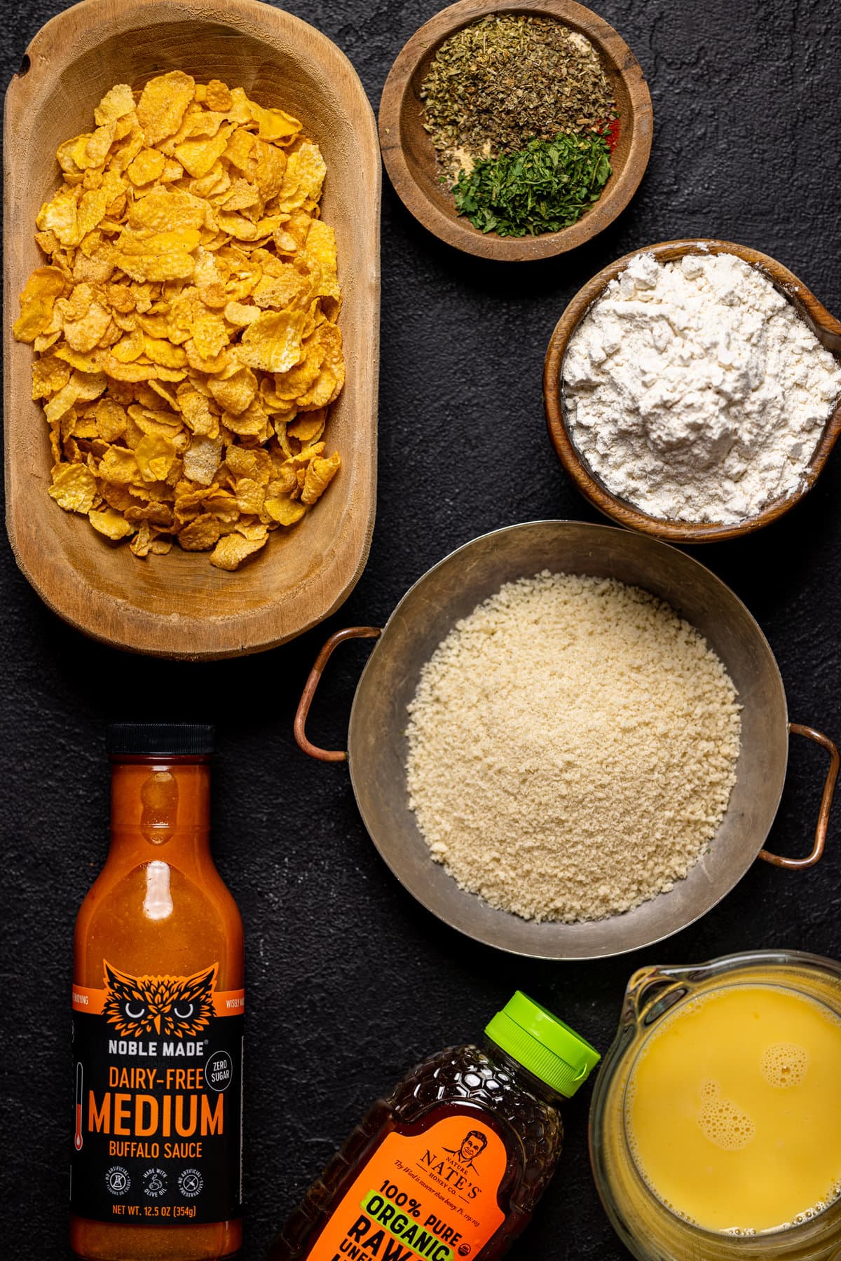 Ingredients for Crispy Buffalo Chicken Tenders including corn flakes, flour, and Noble-Made dairy-free buffalo sauce.