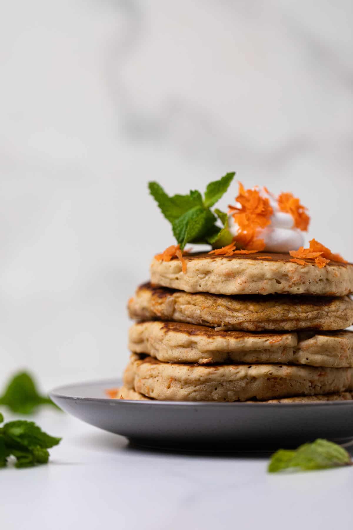 Plate of Easy Vegan Carrot Cake Pancakes in a stack with coconut cream and carrots on top.