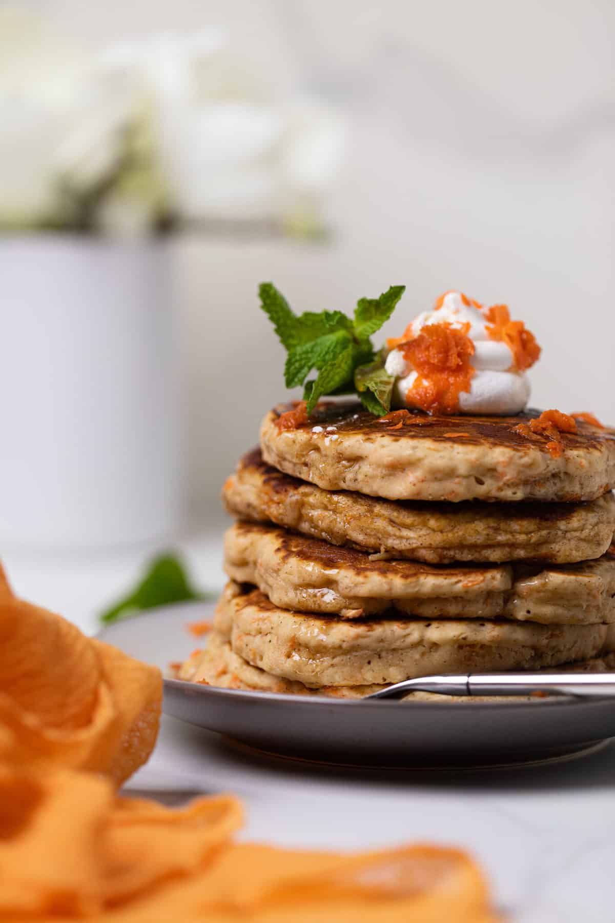 Carrot Cake Pancakes in a stack with coconut cream and carrots on top.