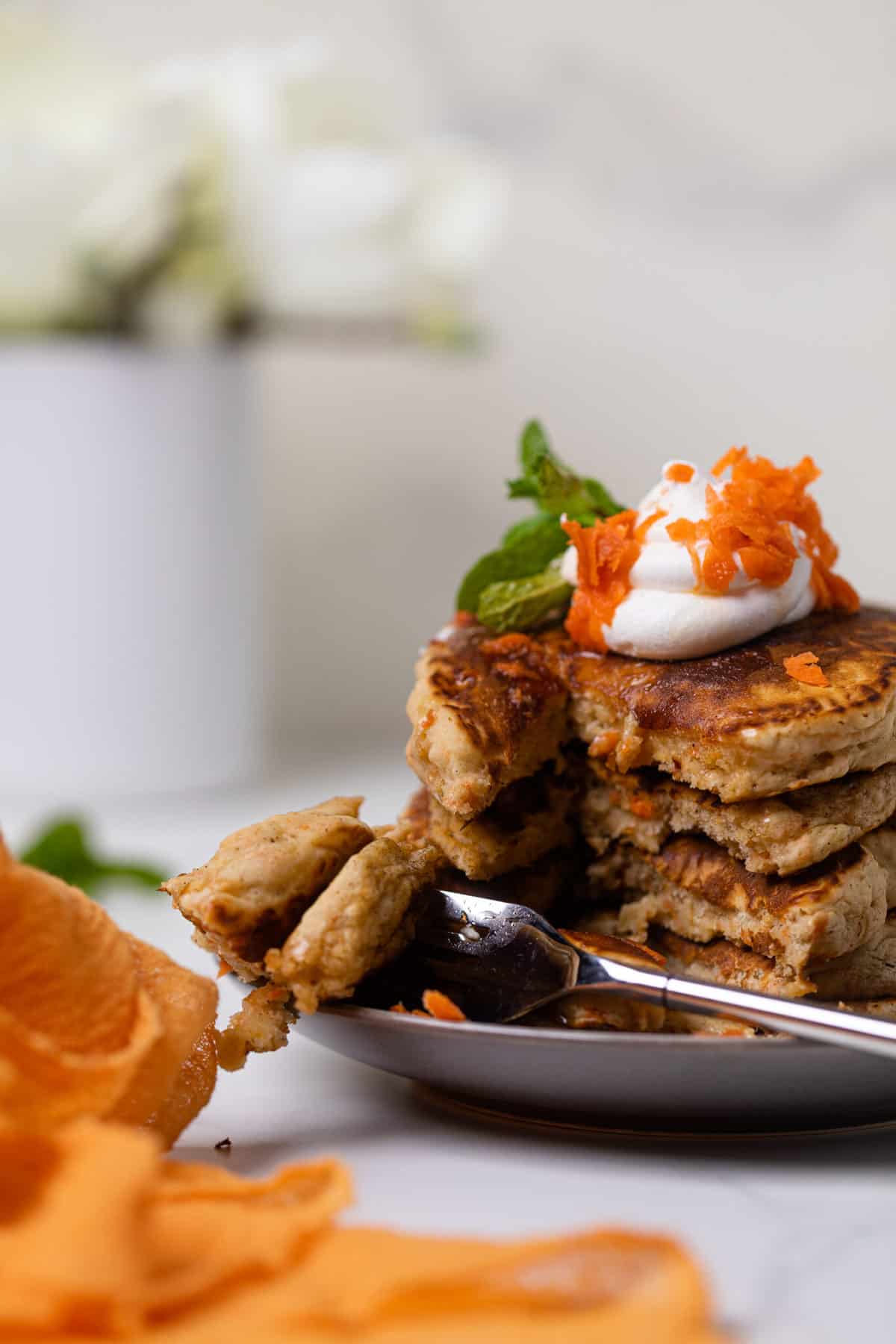 Vegan Carrot Cake Pancakes in a stack topped with coconut cream and carrots.