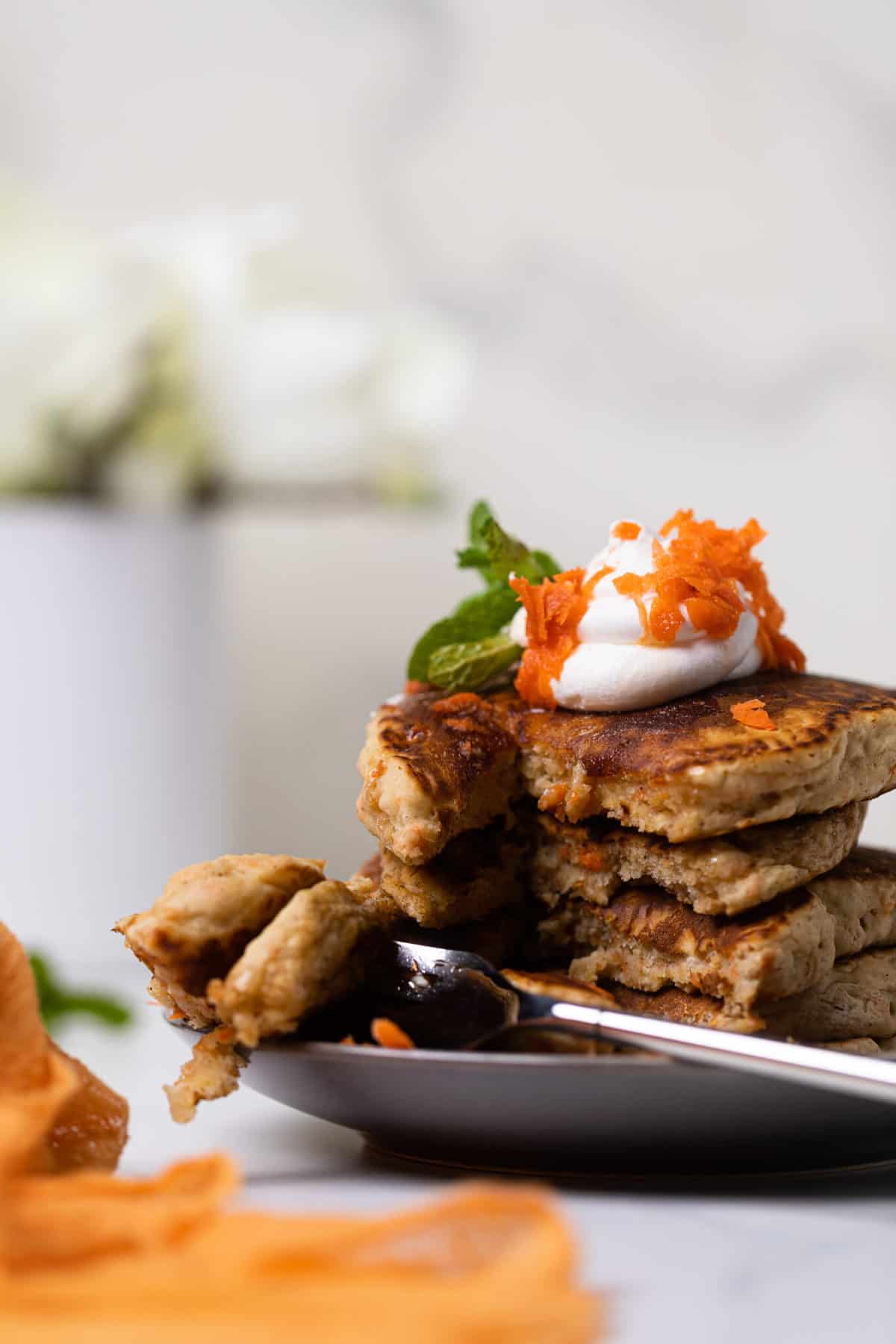 Plate of Easy Vegan Carrot Cake Pancakes in a stack with coconut cream and carrots on top.