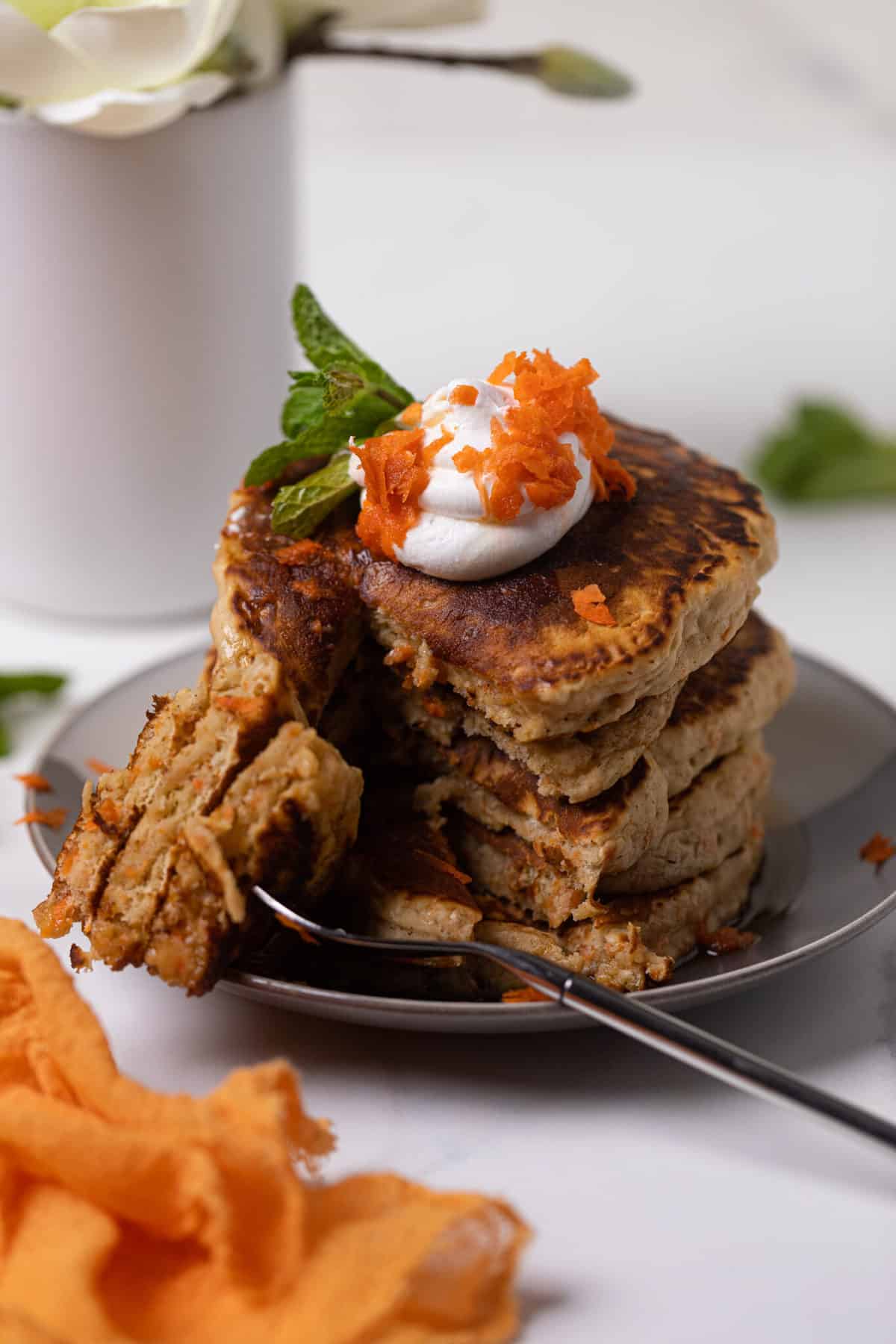 Stack of vegan Carrot Cake Pancakes topped with coconut cream and carrots.