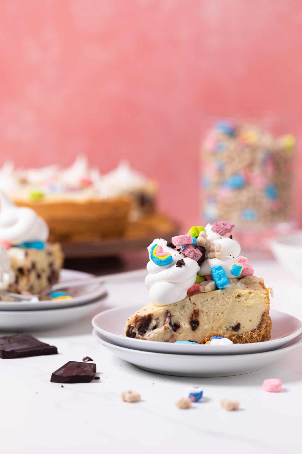 Hunks of chocolate on a table next to a slice of Chocolate Chip Lucky Charms Cheesecake.