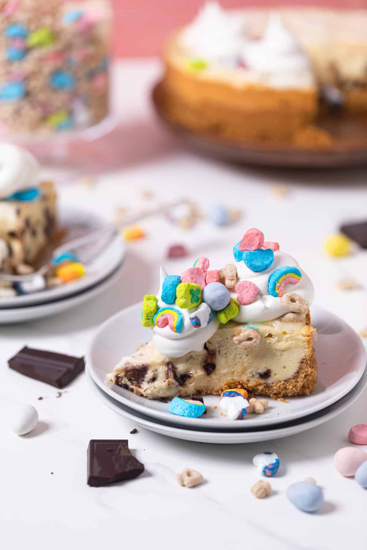 Chocolate Chip Lucky Charms Cheesecake on a plate surrounded by marshmallows and chocolate.