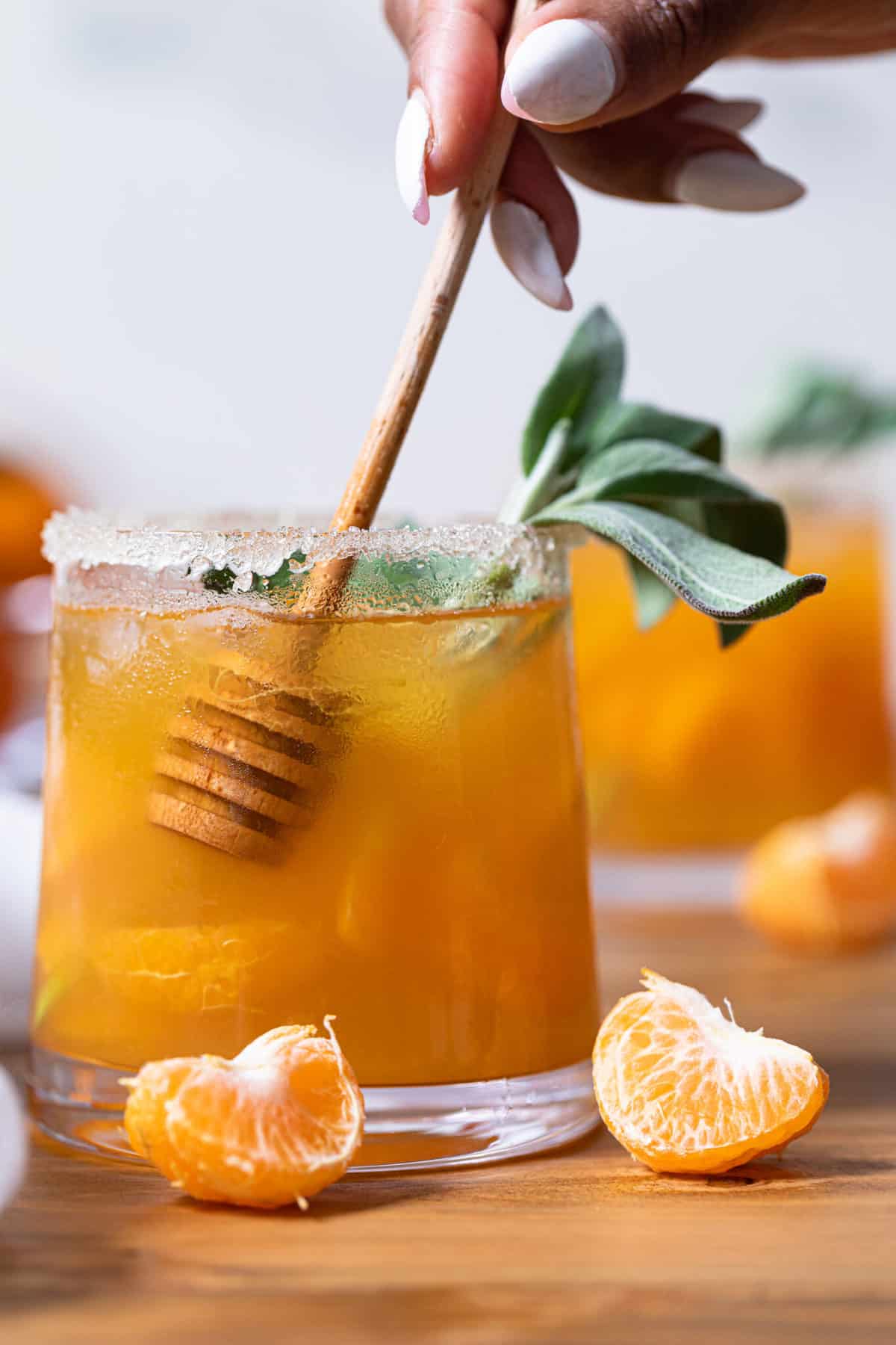 Citrus Honey Sage Drink being stirred with a honey dipper.