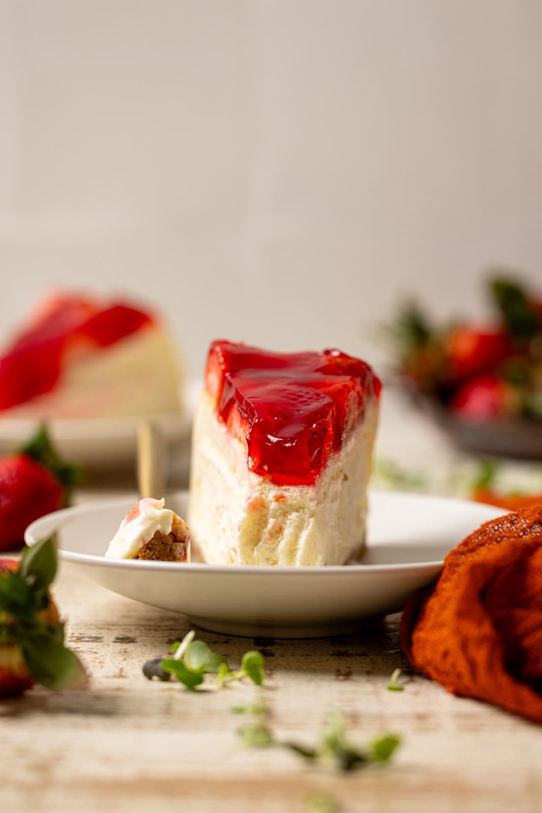 Front shot of slice of cheesecake with a piece removed with a fork and strawberries. 