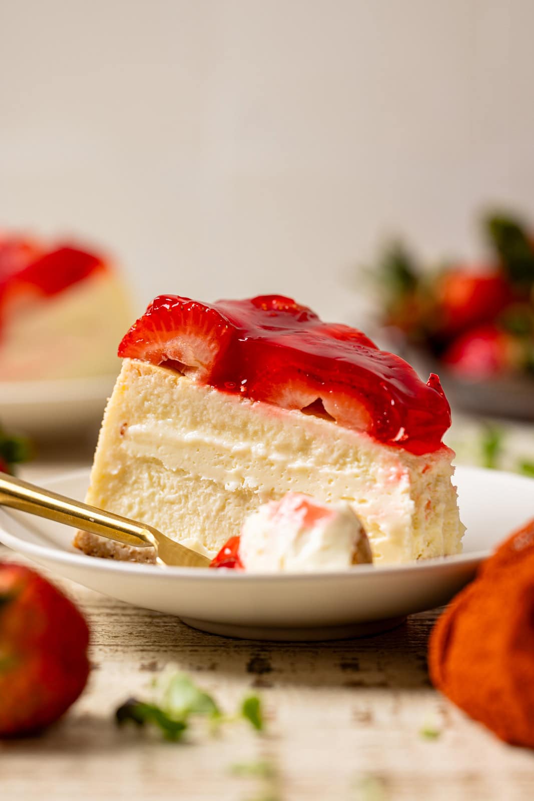 Slice of cheesecake in a plate with a fork and strawberries. 
