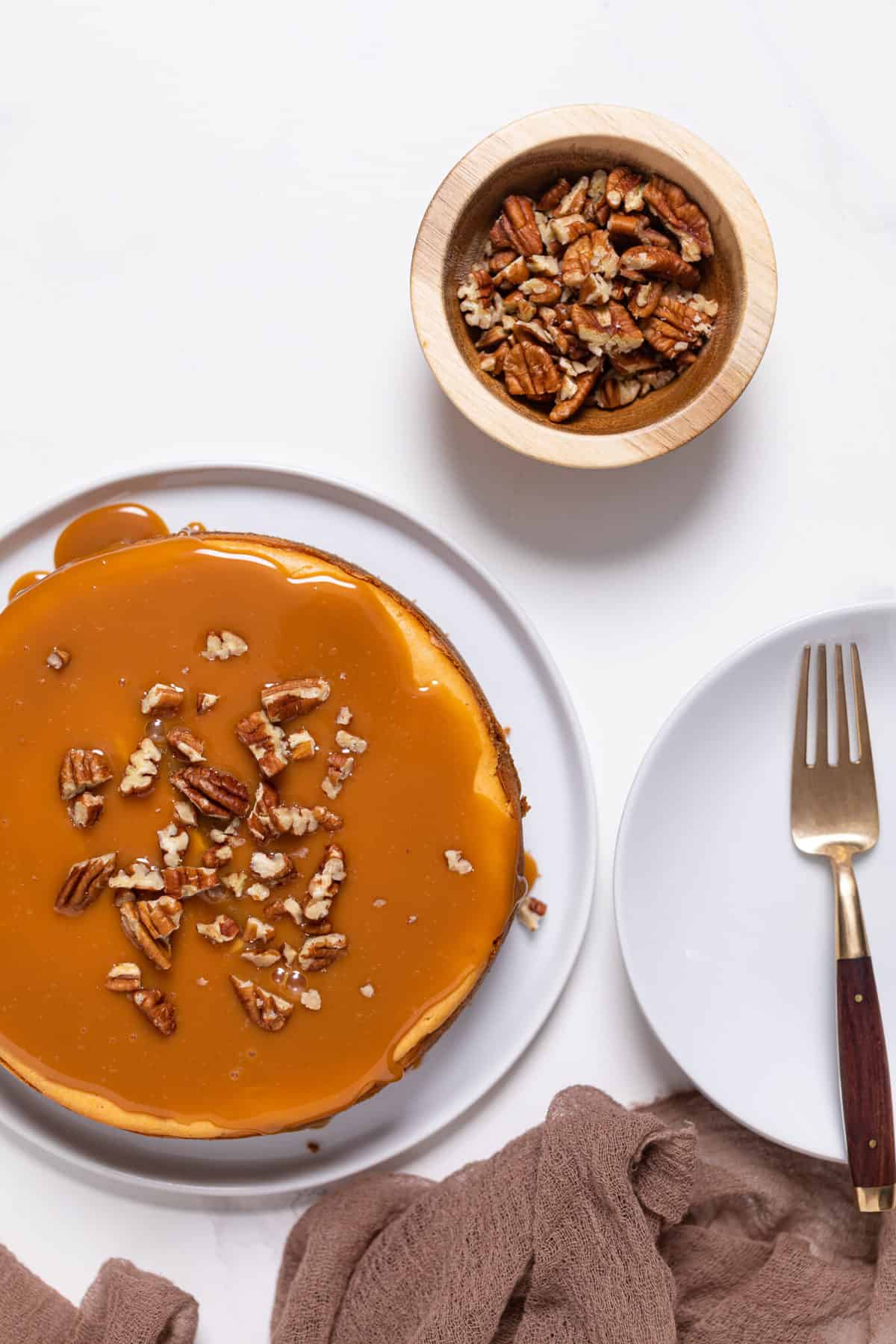 overhead of Sweet Potato Caramel Cheesecake on a white plate with a wooden bowl of chopped nuts on the side