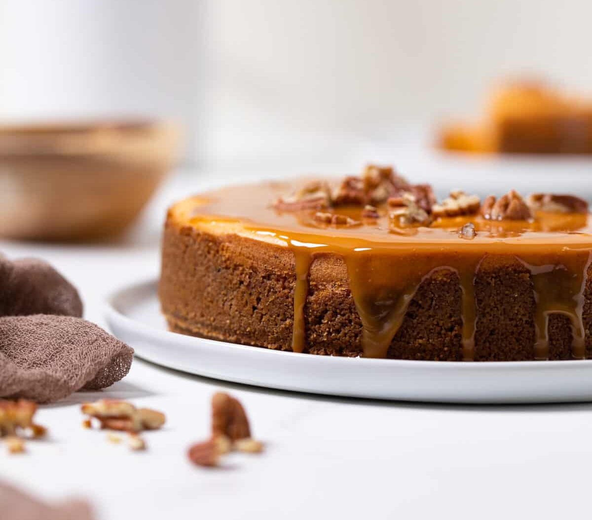 whole Sweet Potato Caramel Cheesecake on a white plate with nuts in the foreground