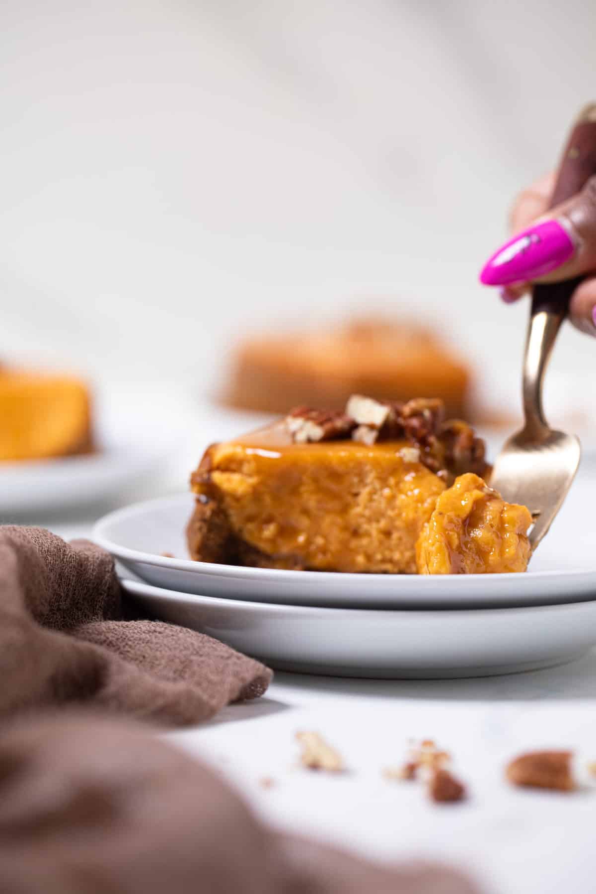 Slice of sweet potato cheesecake with a hand taking a bite on a white plate.