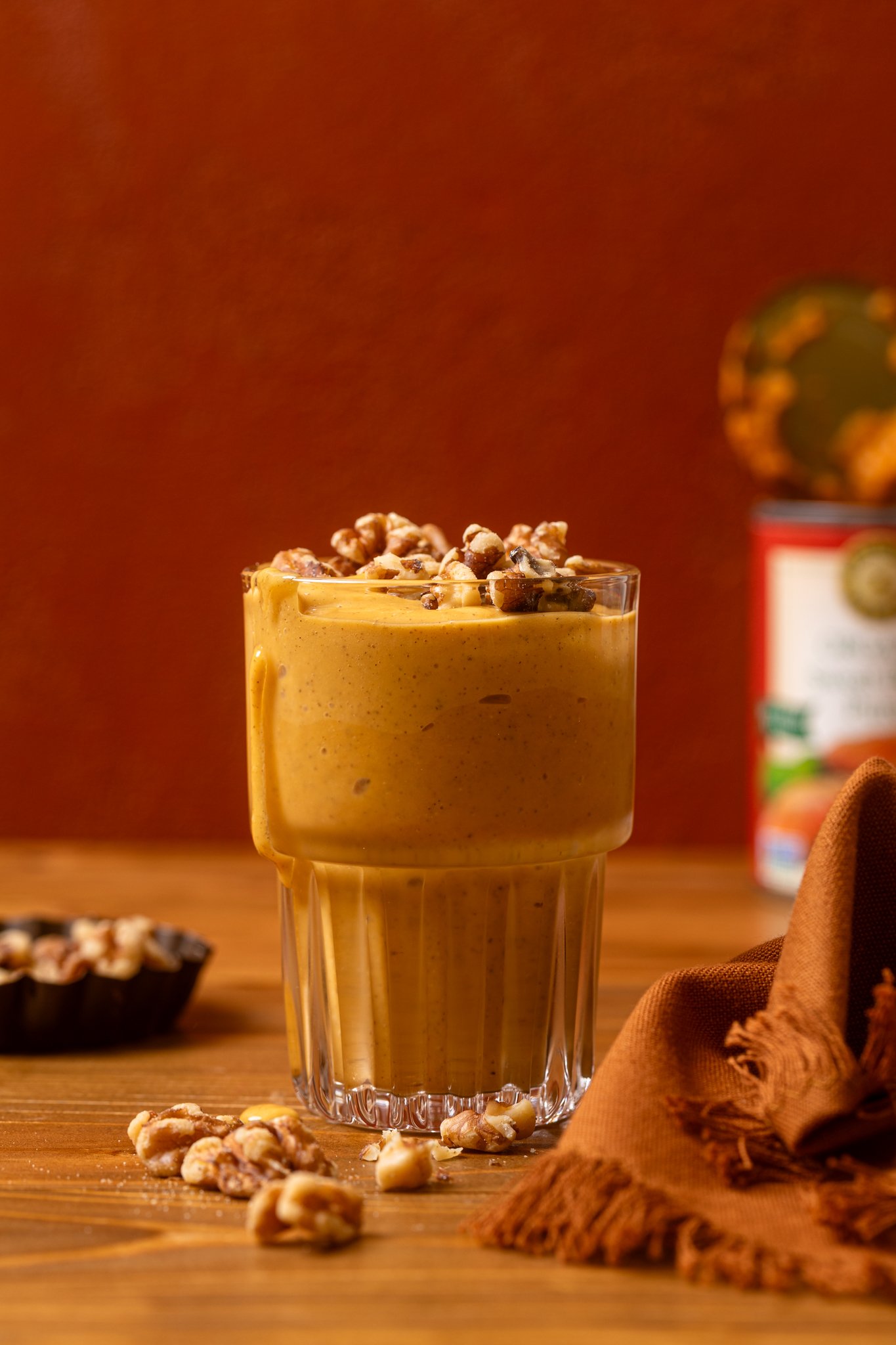 A glass of Cozy Sweet Potato Pie Smoothie with garnish of nuts on a wooden table.