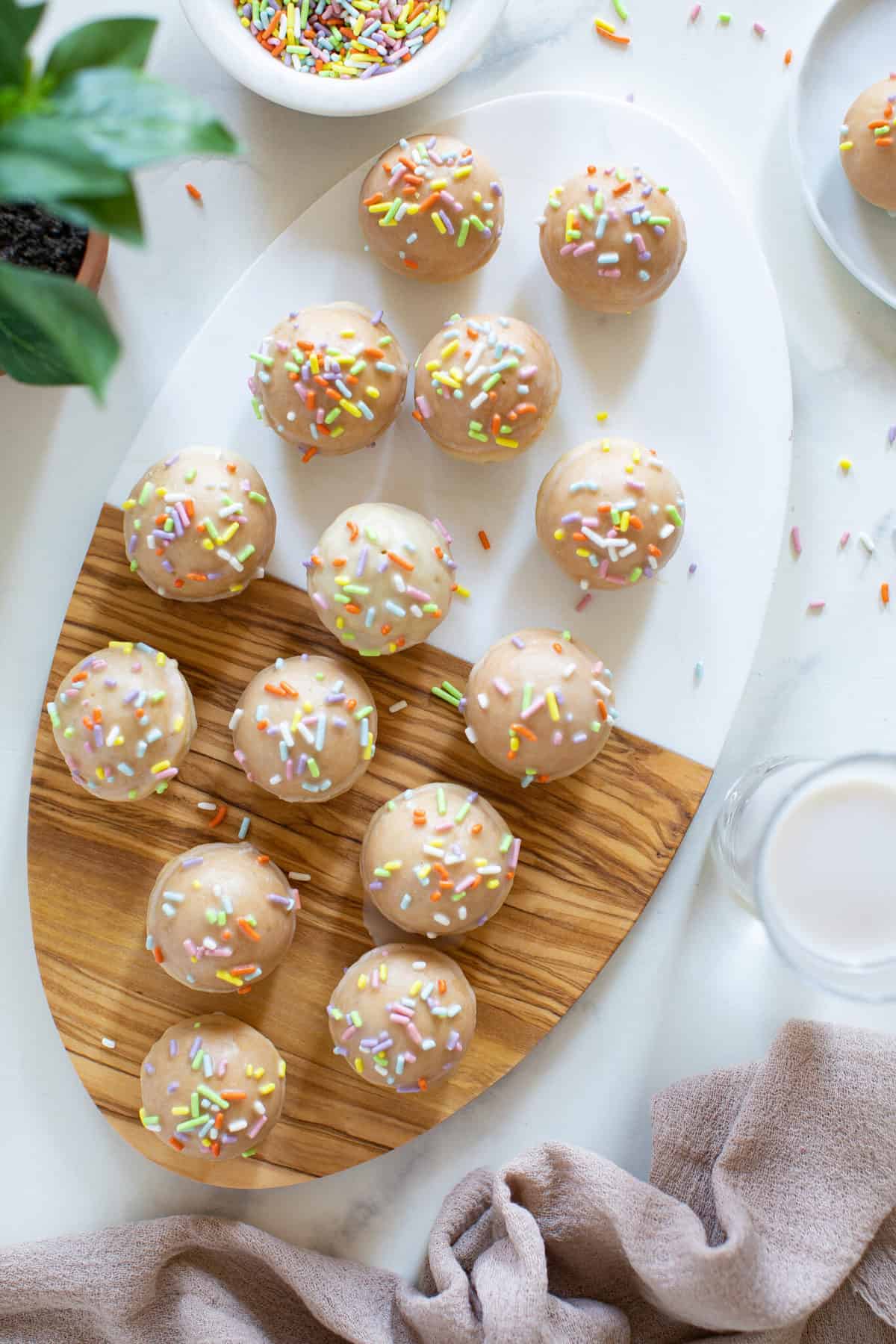 Overhead of cutting board with vegan sprinkle donut holes with rainbow sprinkles.