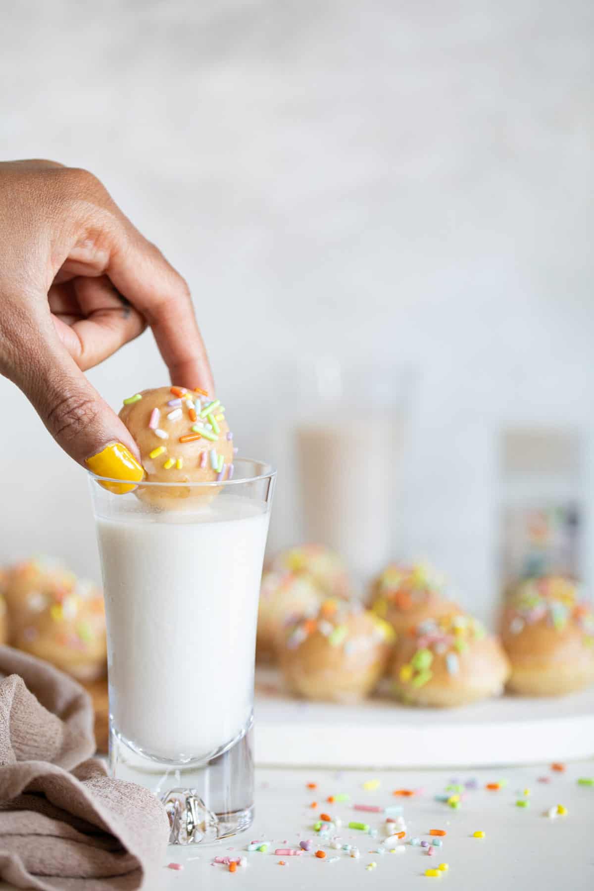 Hand dipping a homemade donut hole in a glass of milk.