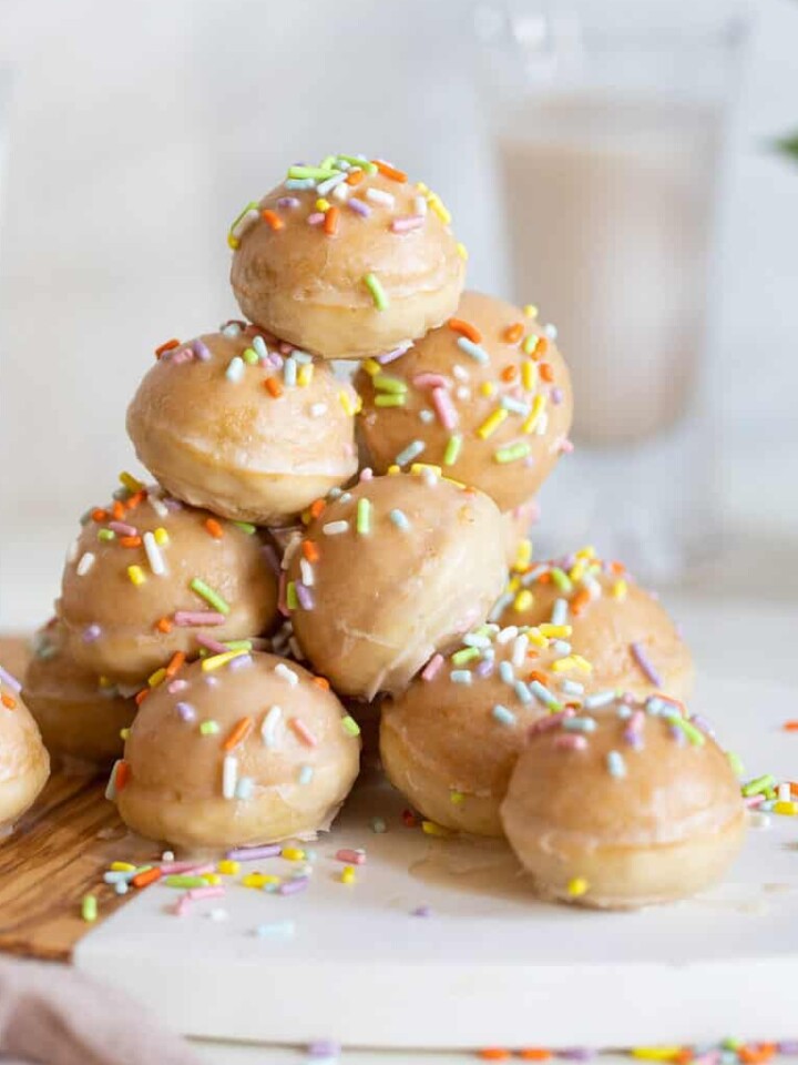 Stack of vegan donut holes with sprinkles and vanilla glaze on a cutting board.