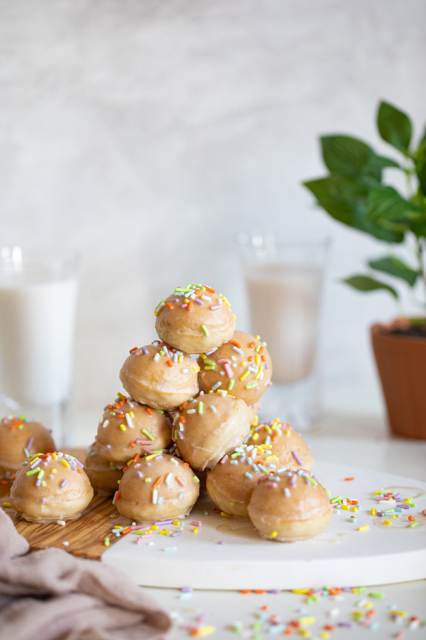 Stack of vegan donut holes with sprinkles and vanilla glaze on a cutting board.