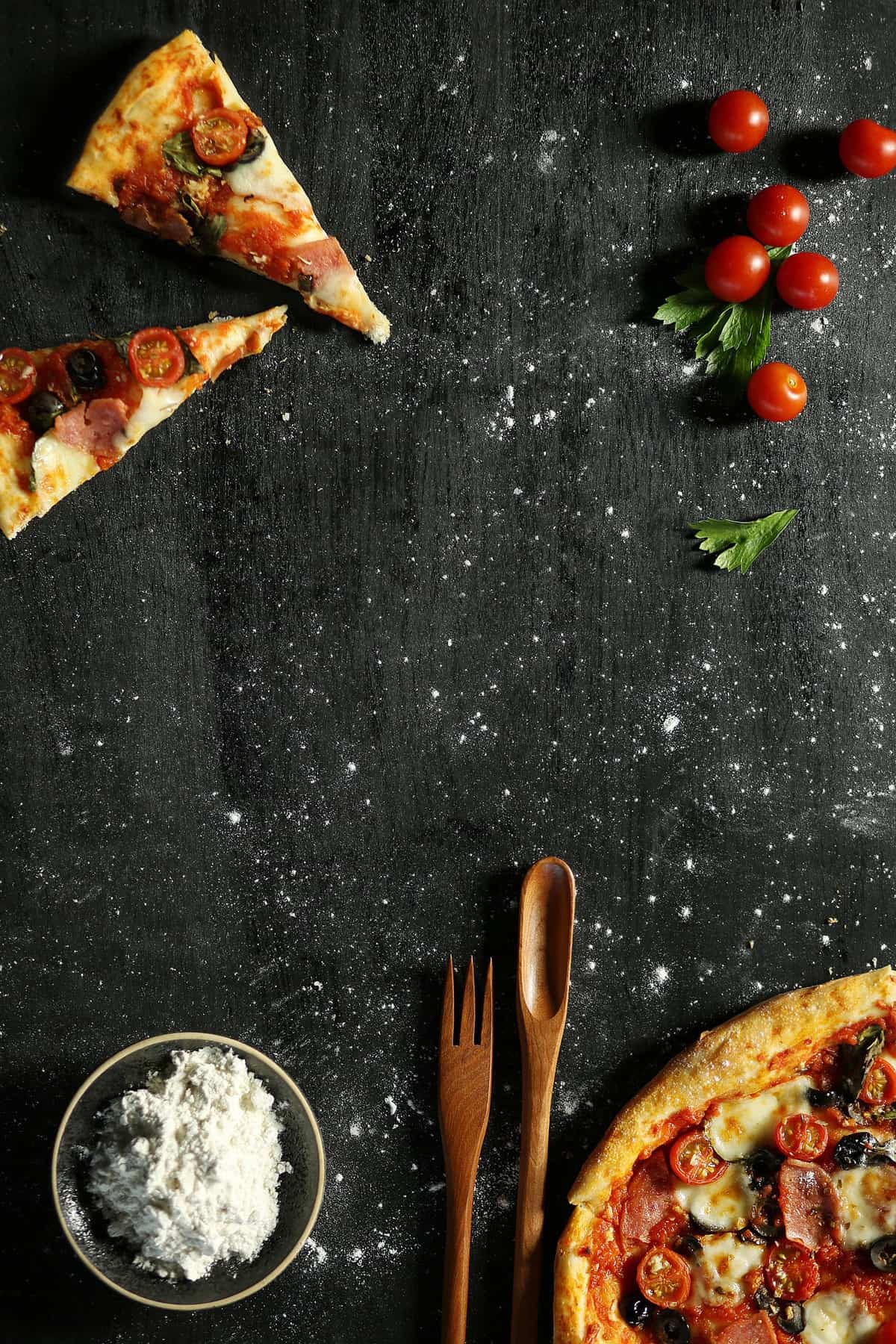 Pizza and tomatoes on a black surface.