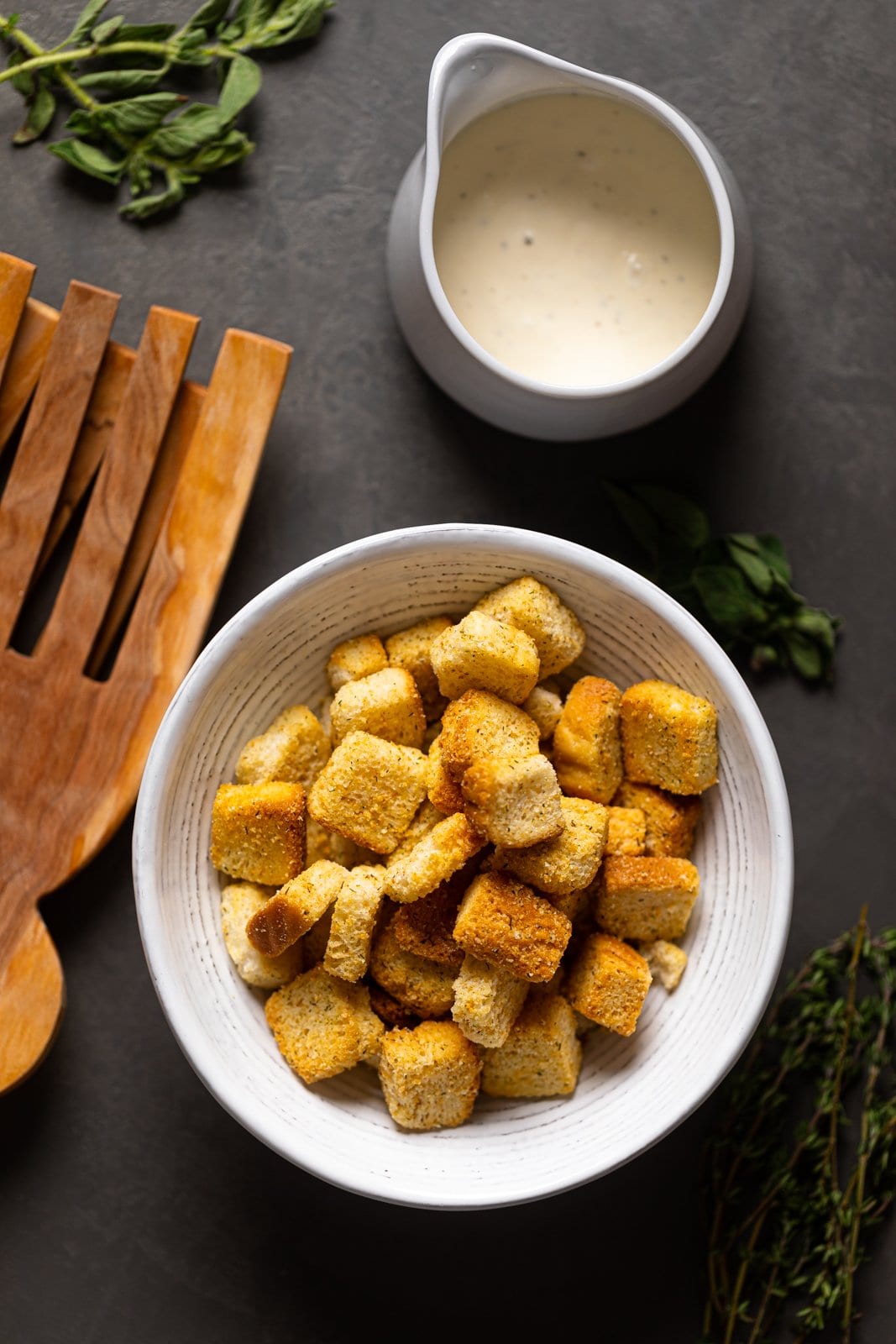 Bowl of croutons next to a jar of garlic dressing and wooden salad tossers