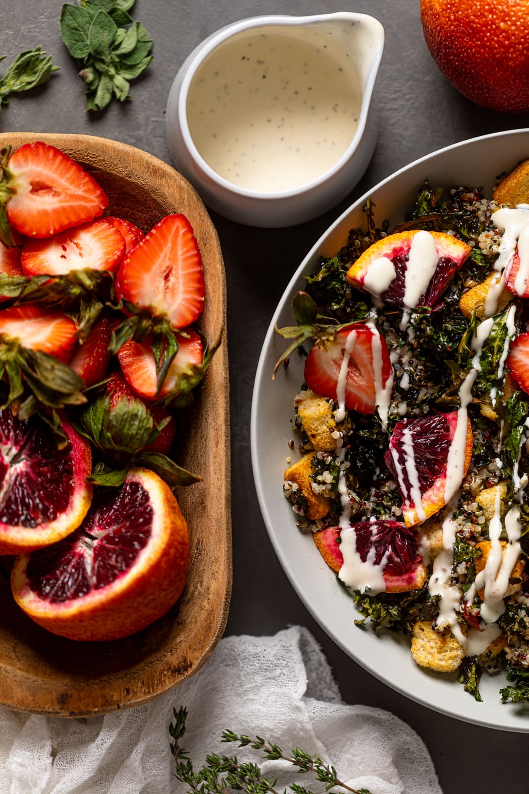 Bowl of Blood Orange Kale Salad near a jar of garlic dressing and bowl of halved strawberries and blood orange