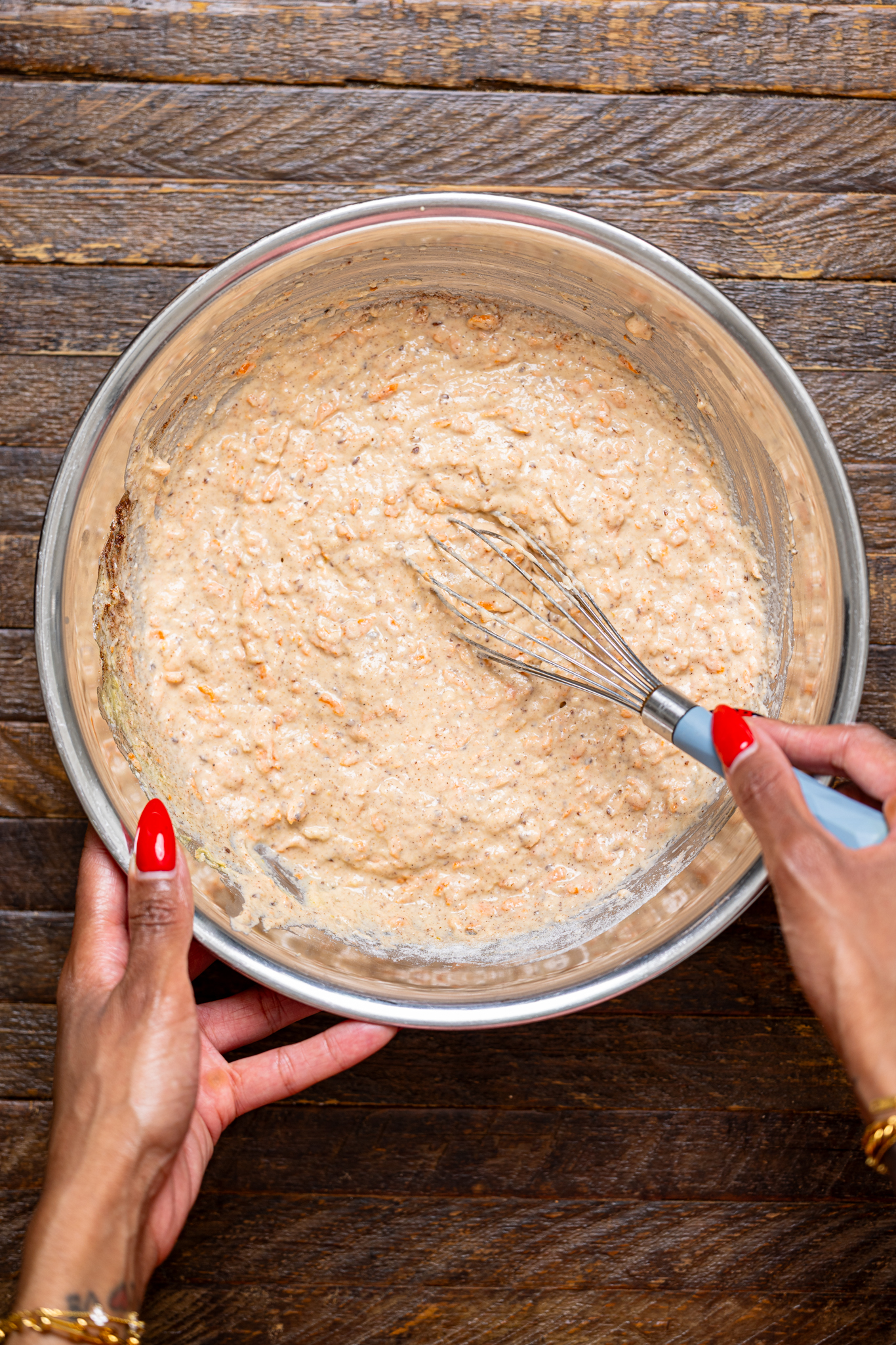 The pancake batter in a silver bowl being whisked with women hands.